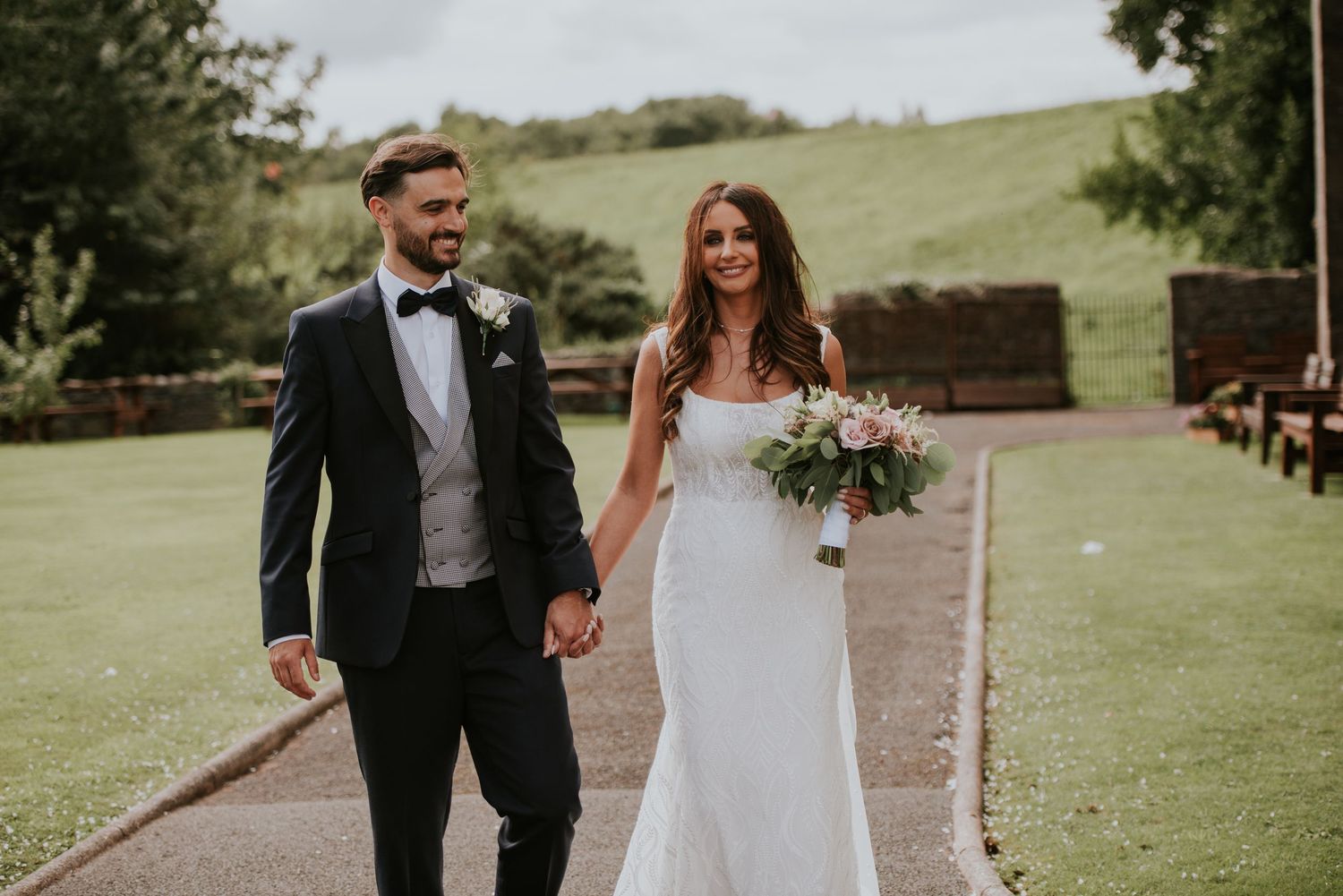 Wedding couple walking together on lush green grounds during outdoor ceremony.