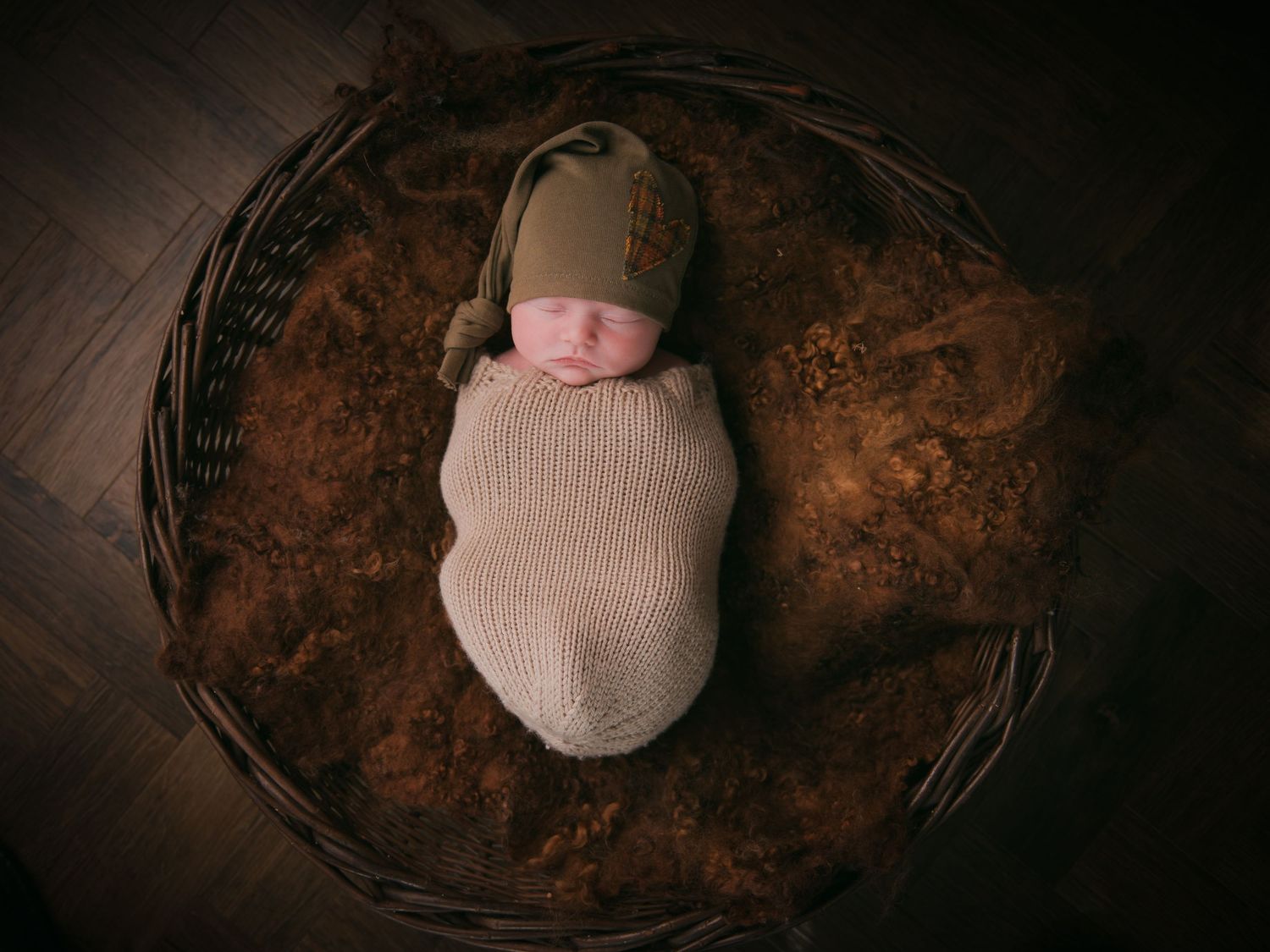 Sleeping newborn in dark rustic basket with moody lighting.