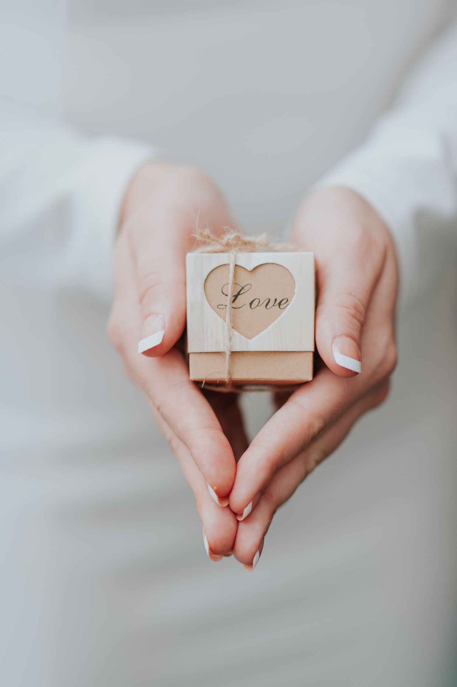 A sequence of hands holding small kraft paper boxes with string and love text against a light background.