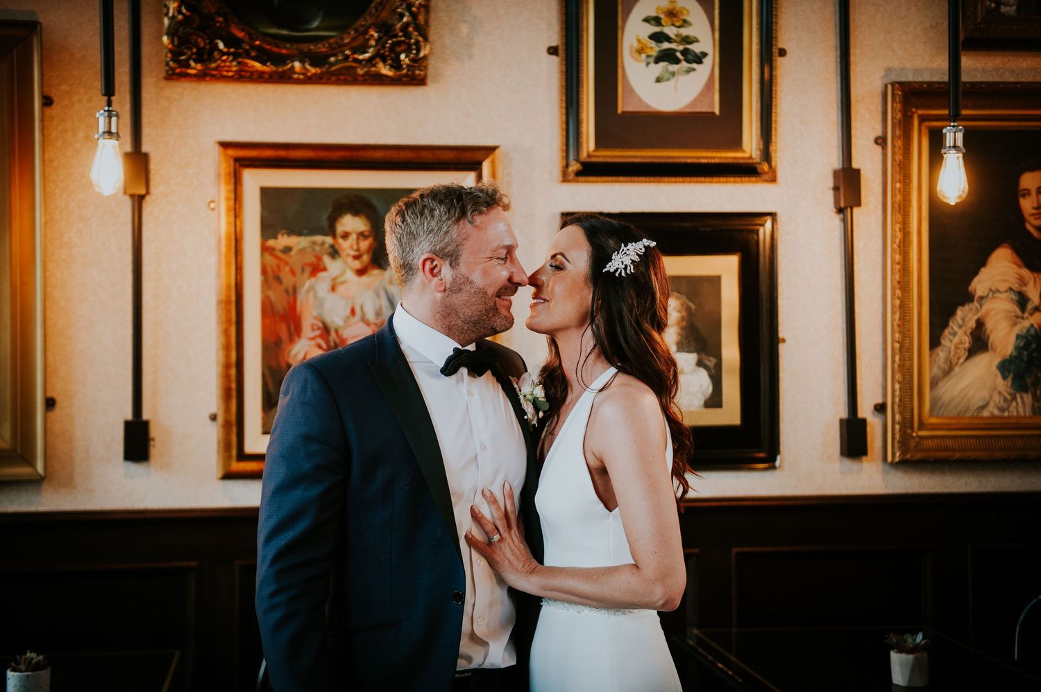 Intimate wedding moments photographed in warm-lit room with vintage decor and artwork.