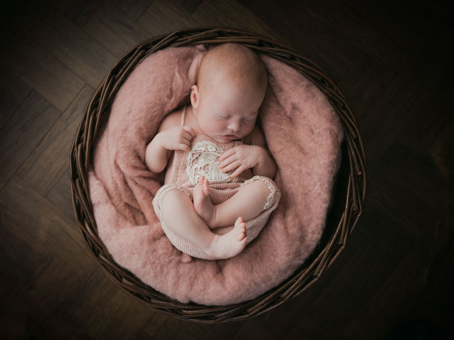 Newborn baby sleeping peacefully in round woven basket.