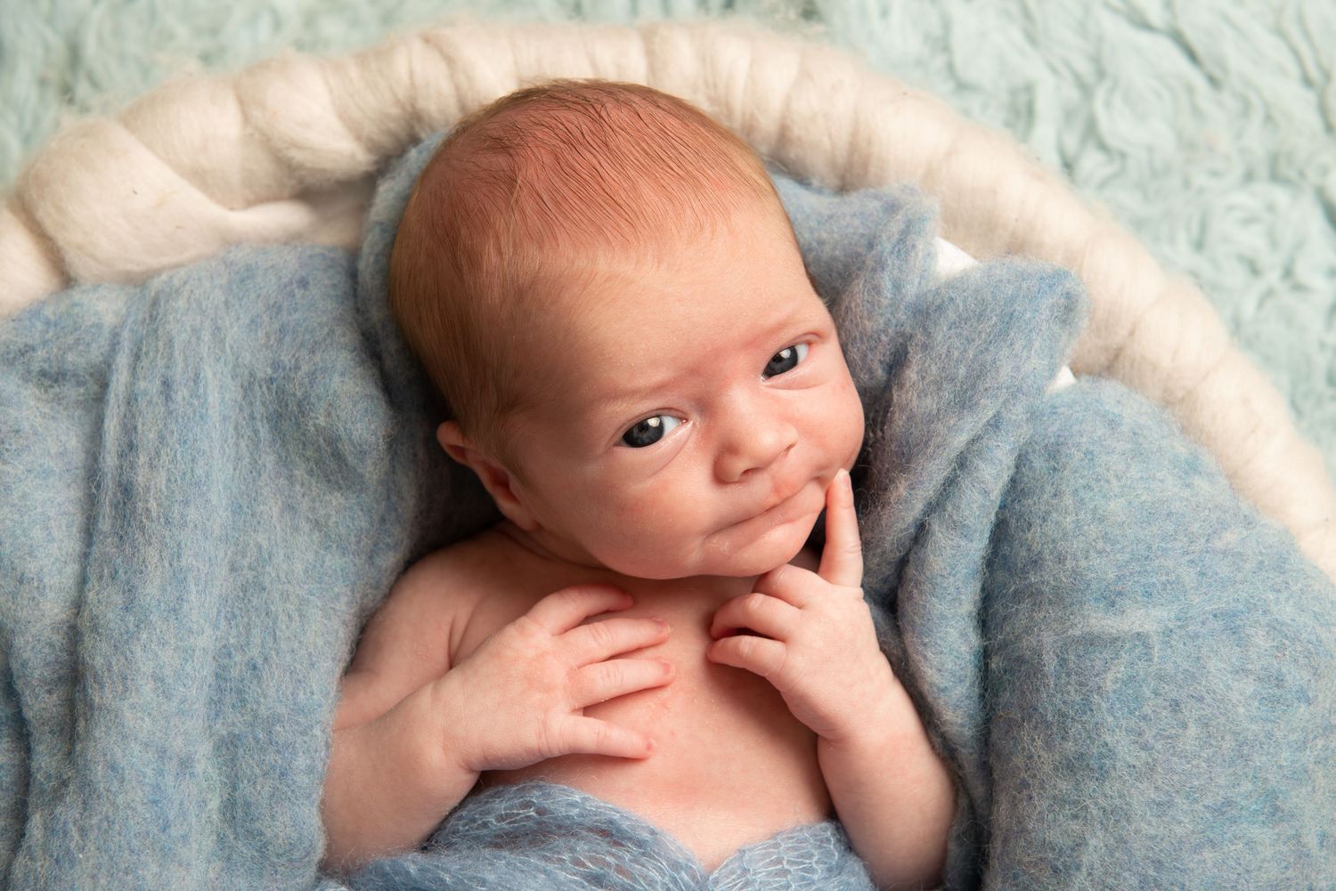 Baby wrapped in soft blue blanket smiling while lying on textured background.