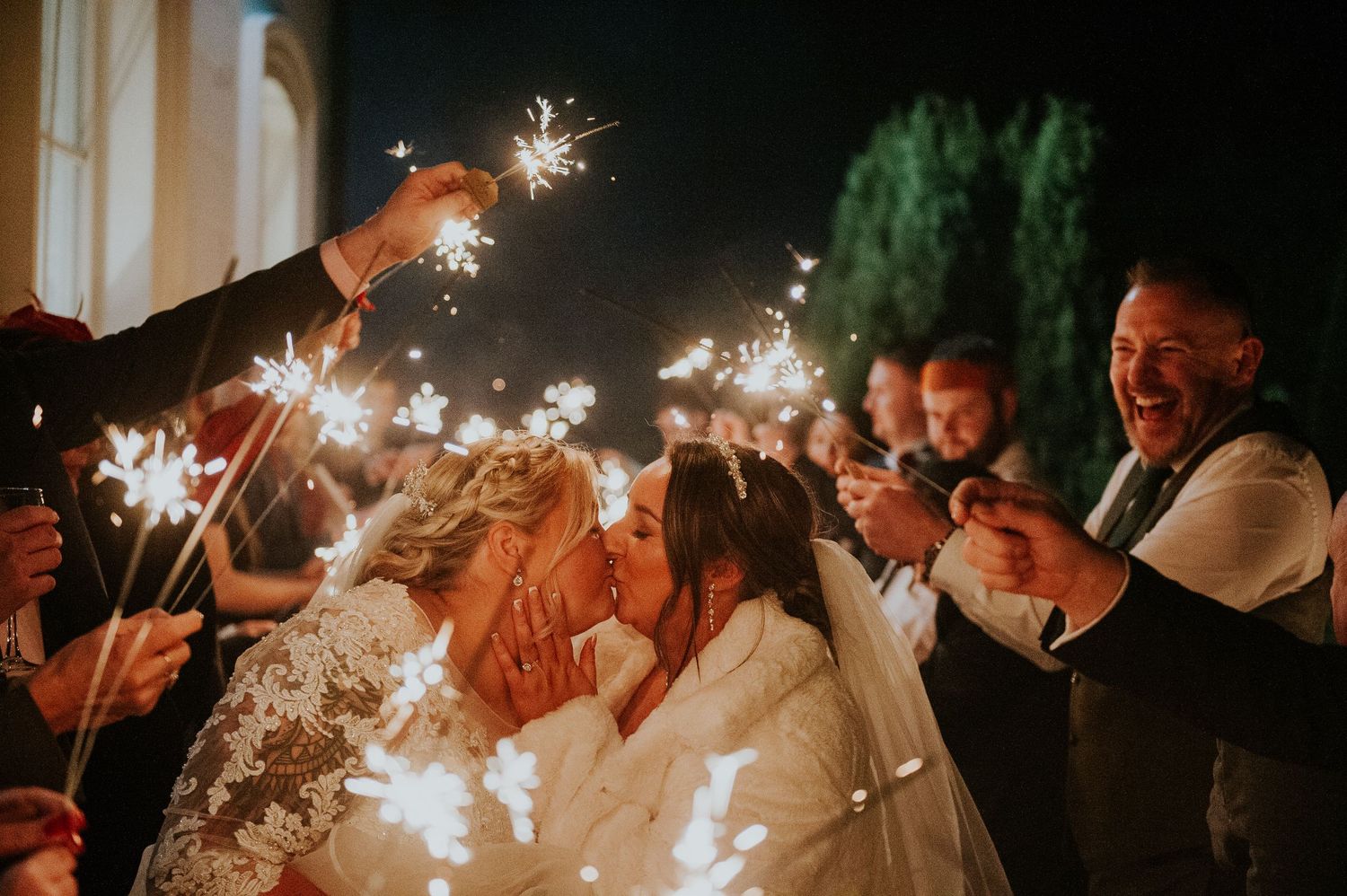 Wedding guests hold sparklers creating a magical nighttime celebration atmosphere.