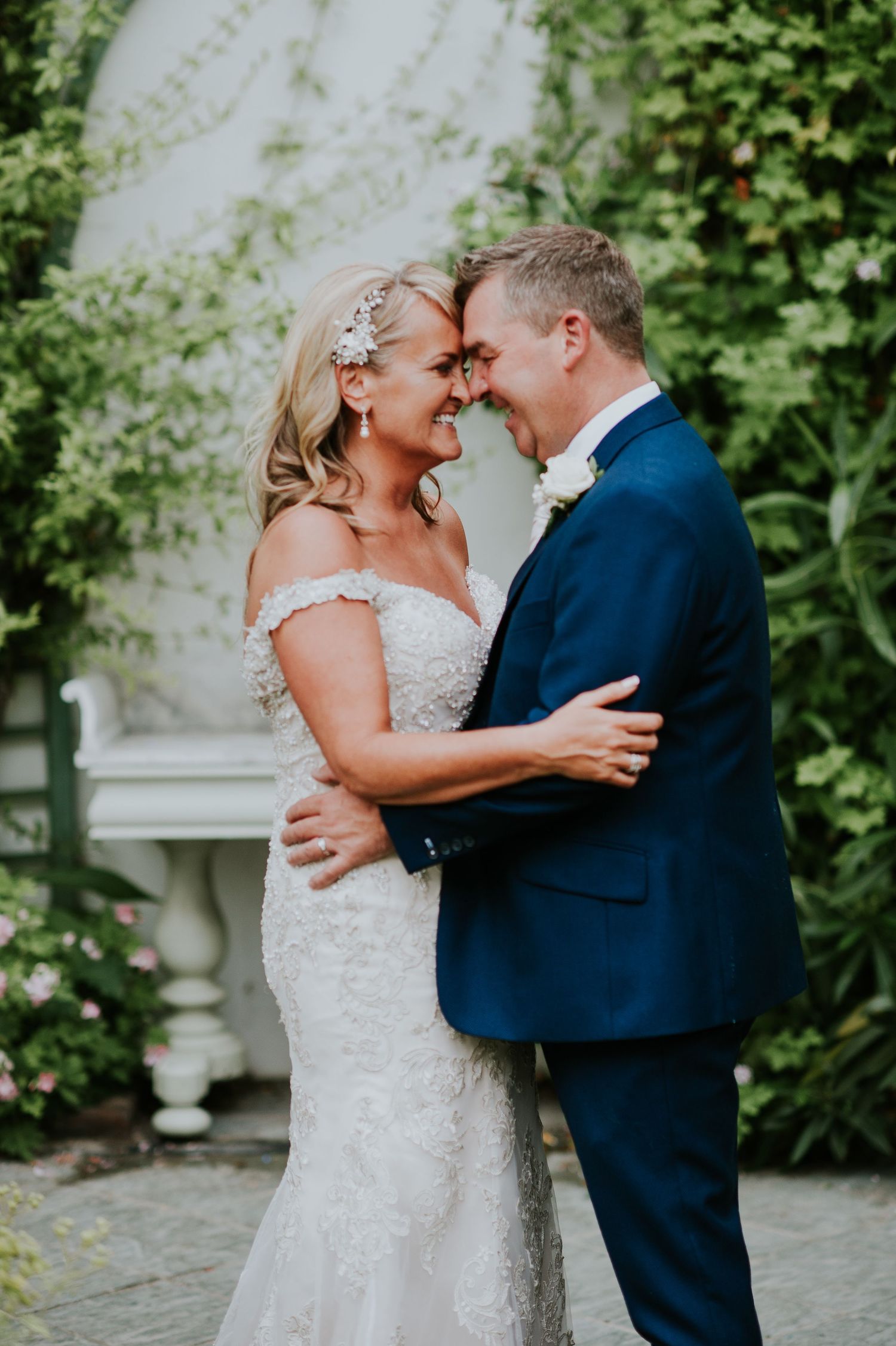 Romantic wedding couple embracing against lush garden backdrop.