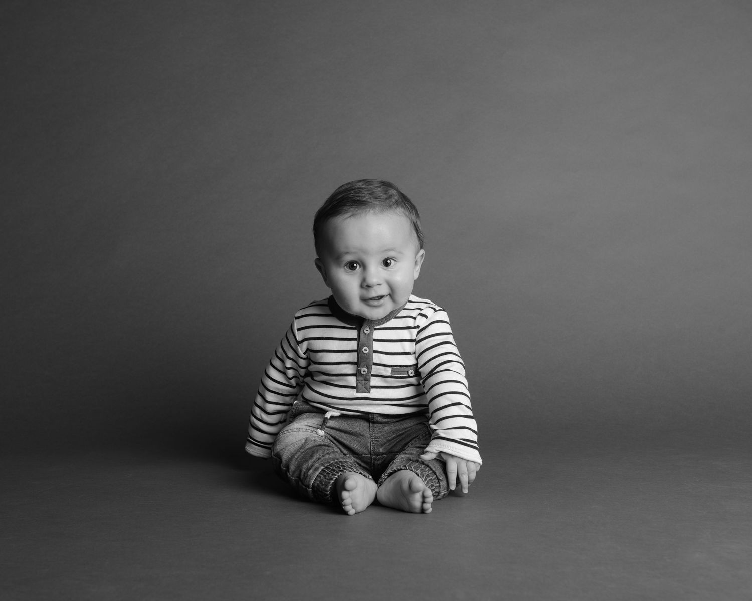 Series of black and white portraits showing baby milestones on gray background.