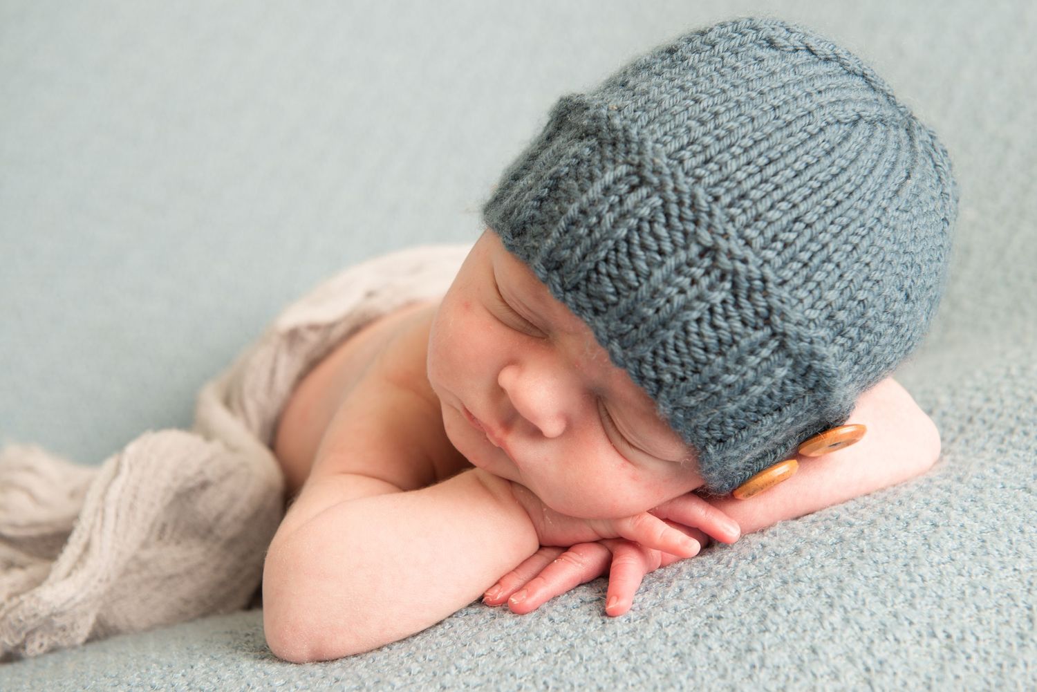 Sleeping newborn wearing knit hat on soft gray blanket.