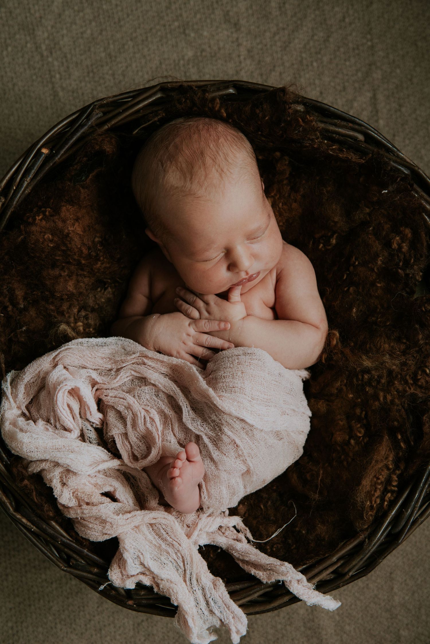 Newborn baby sleeping peacefully wrapped in soft white fabric in a dark wooden bowl.