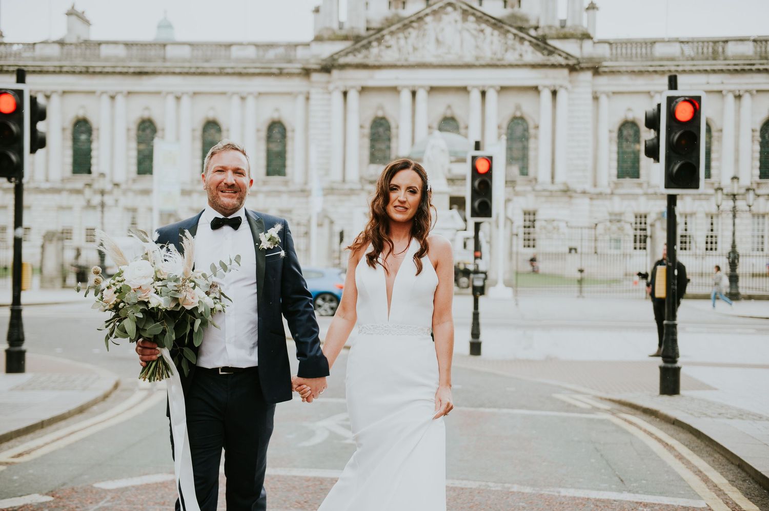 Wedding party walking along ornate classical building exterior with decorative details.