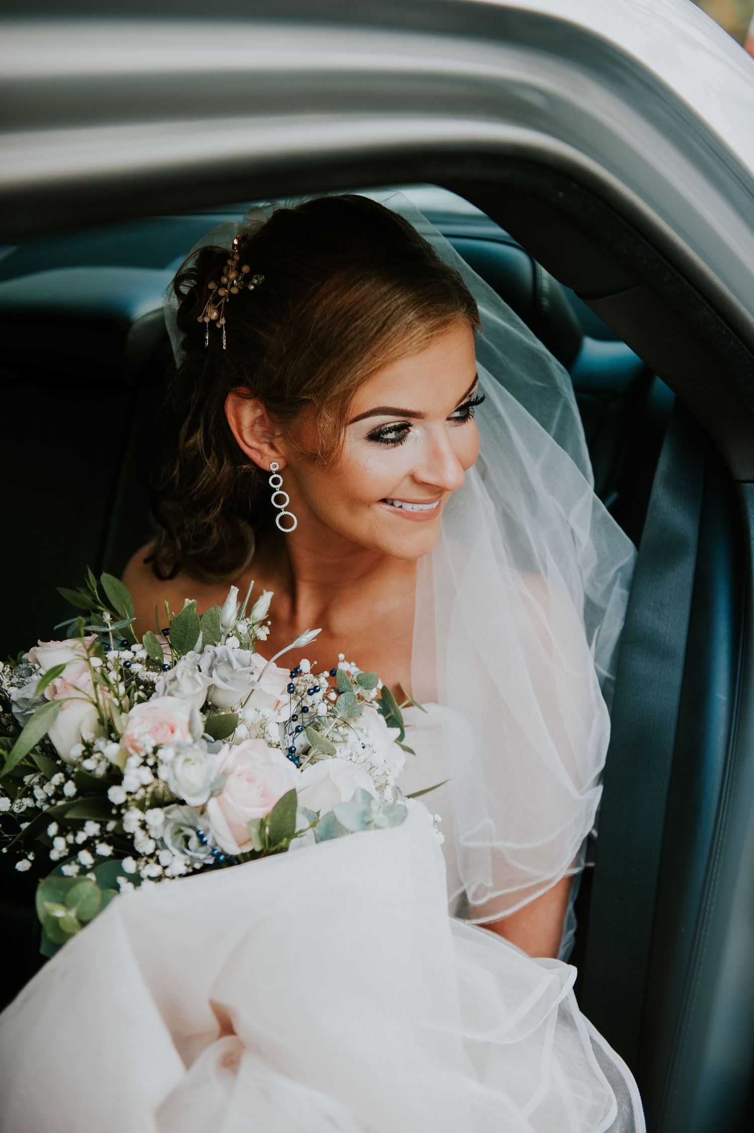 Bride sitting in car with white bouquet and flowing veil.