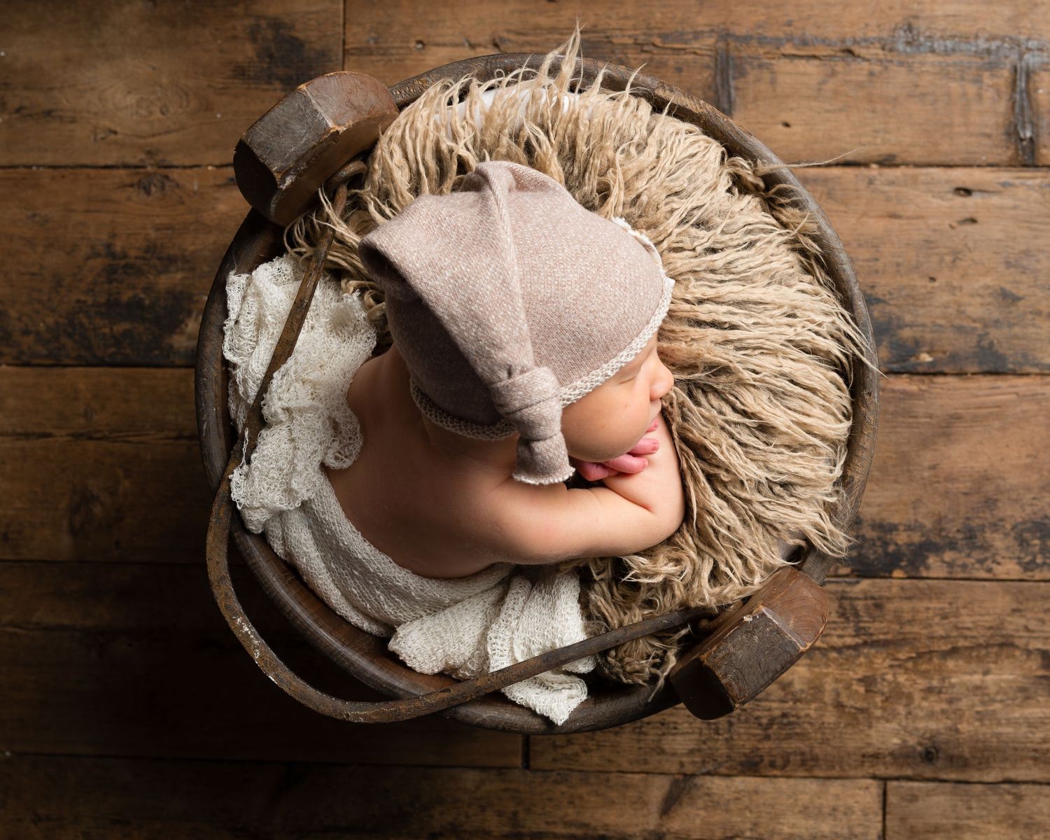 Artistic overhead view of baby lying on textured beige blanket against wooden background.
