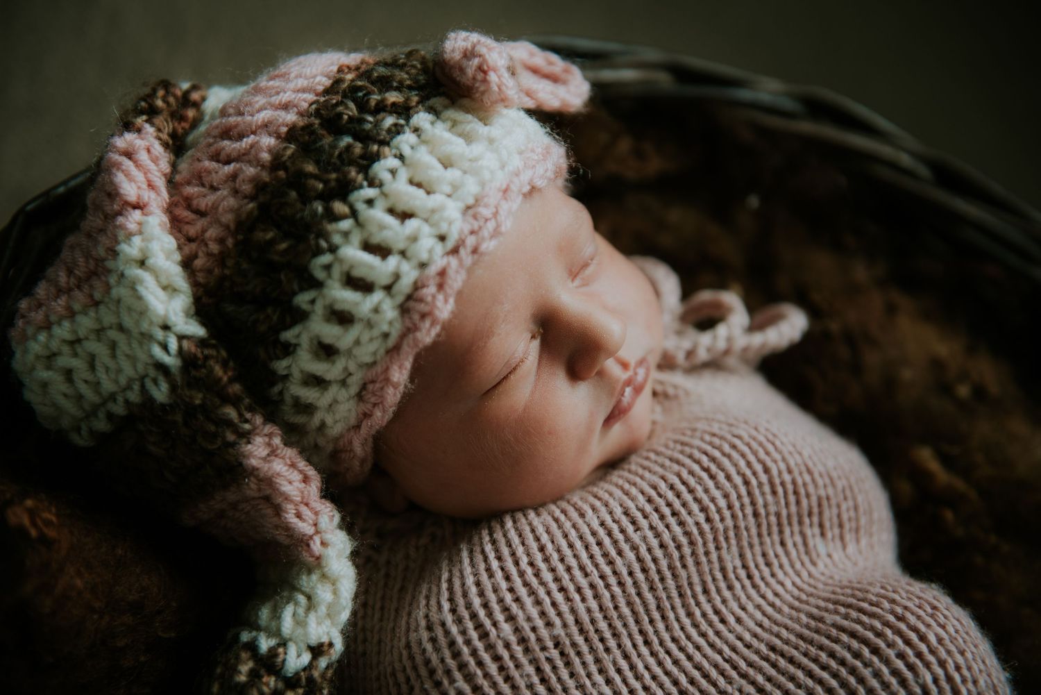 Sleeping newborn wrapped in knitted blanket and wearing delicate lace headband.