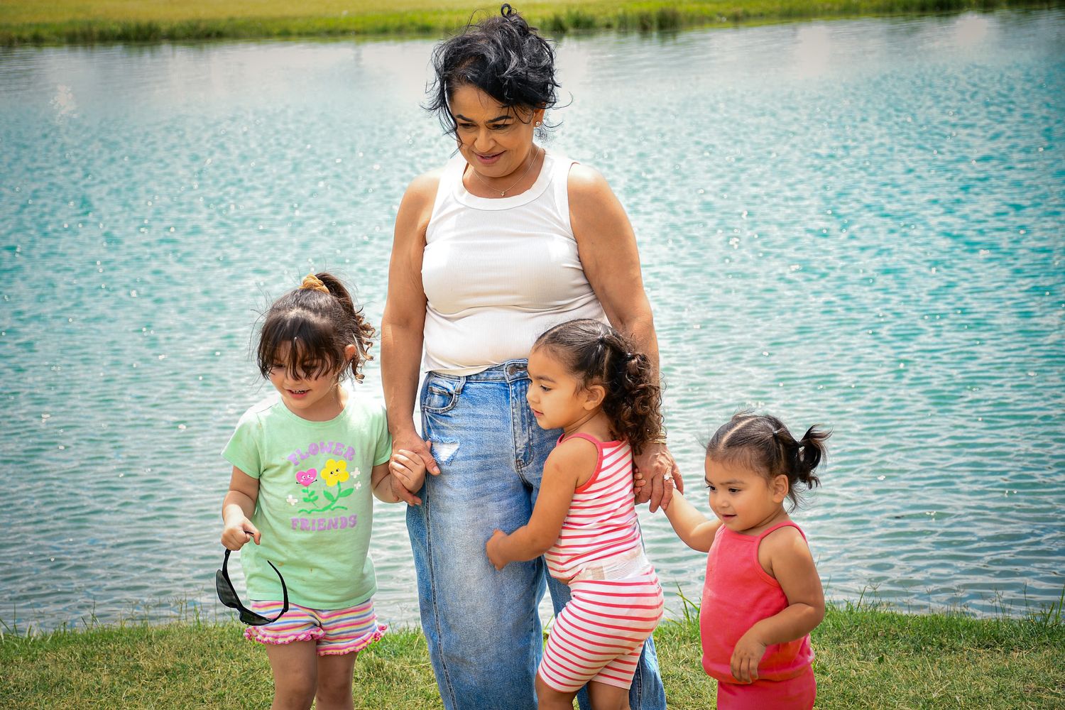 A group stands together by a tranquil lake with green grass on a sunny day.