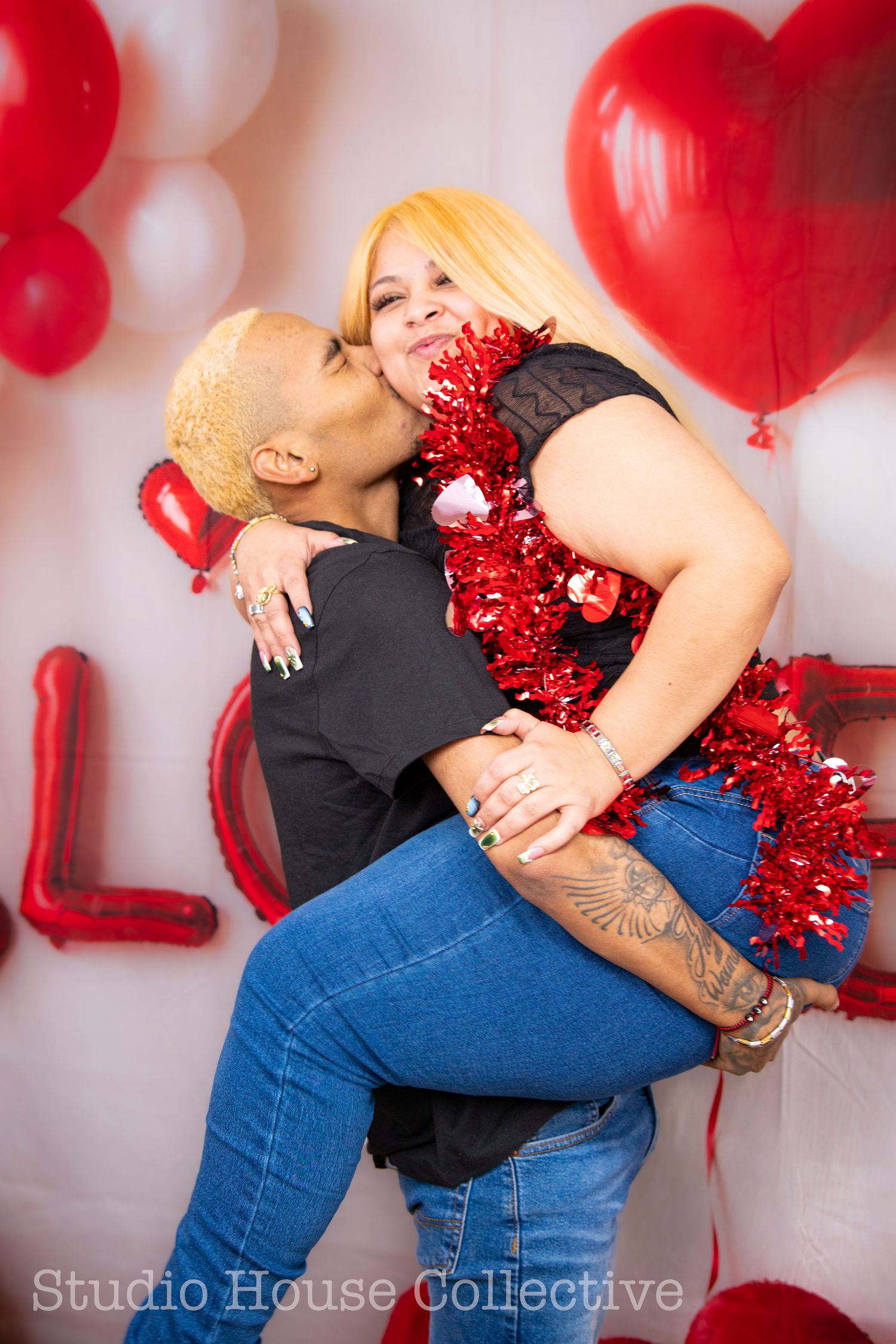 Romantic Valentine's day photoshoot with red balloons and couple embracing against white backdrop.