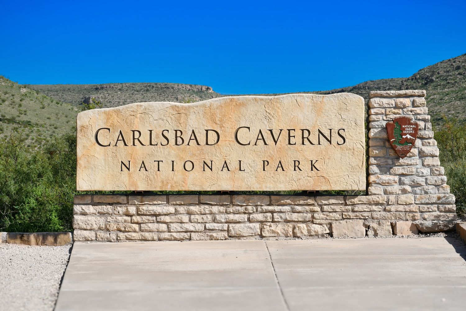 Stone entrance sign for Carlsbad Caverns National Park against a bright blue desert sky.