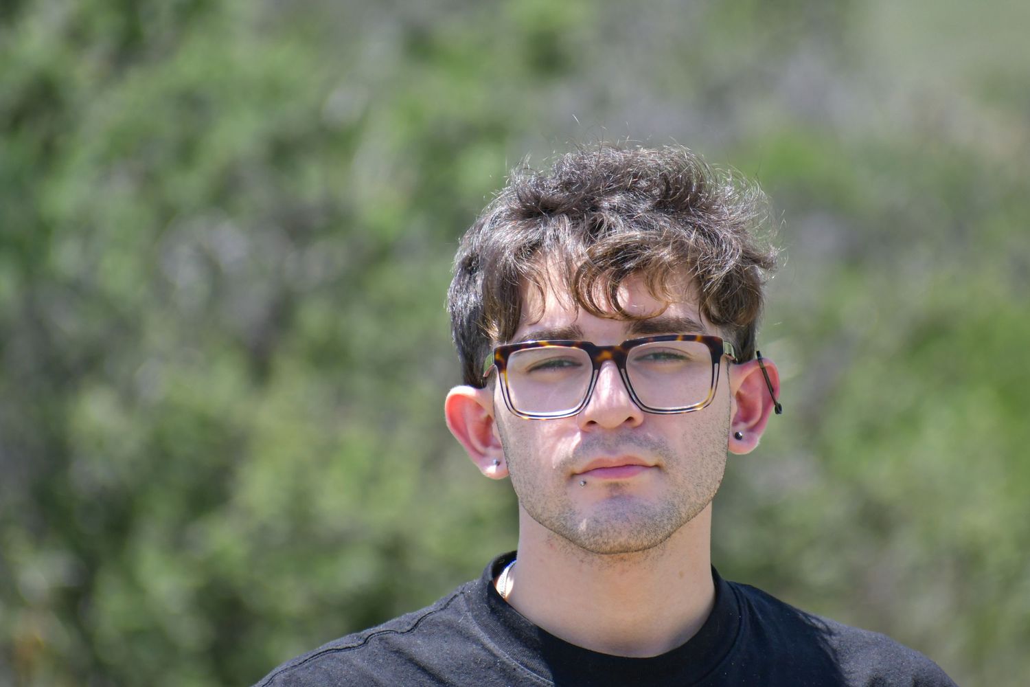 Portrait of someone wearing glasses in a natural outdoor setting with green foliage background.