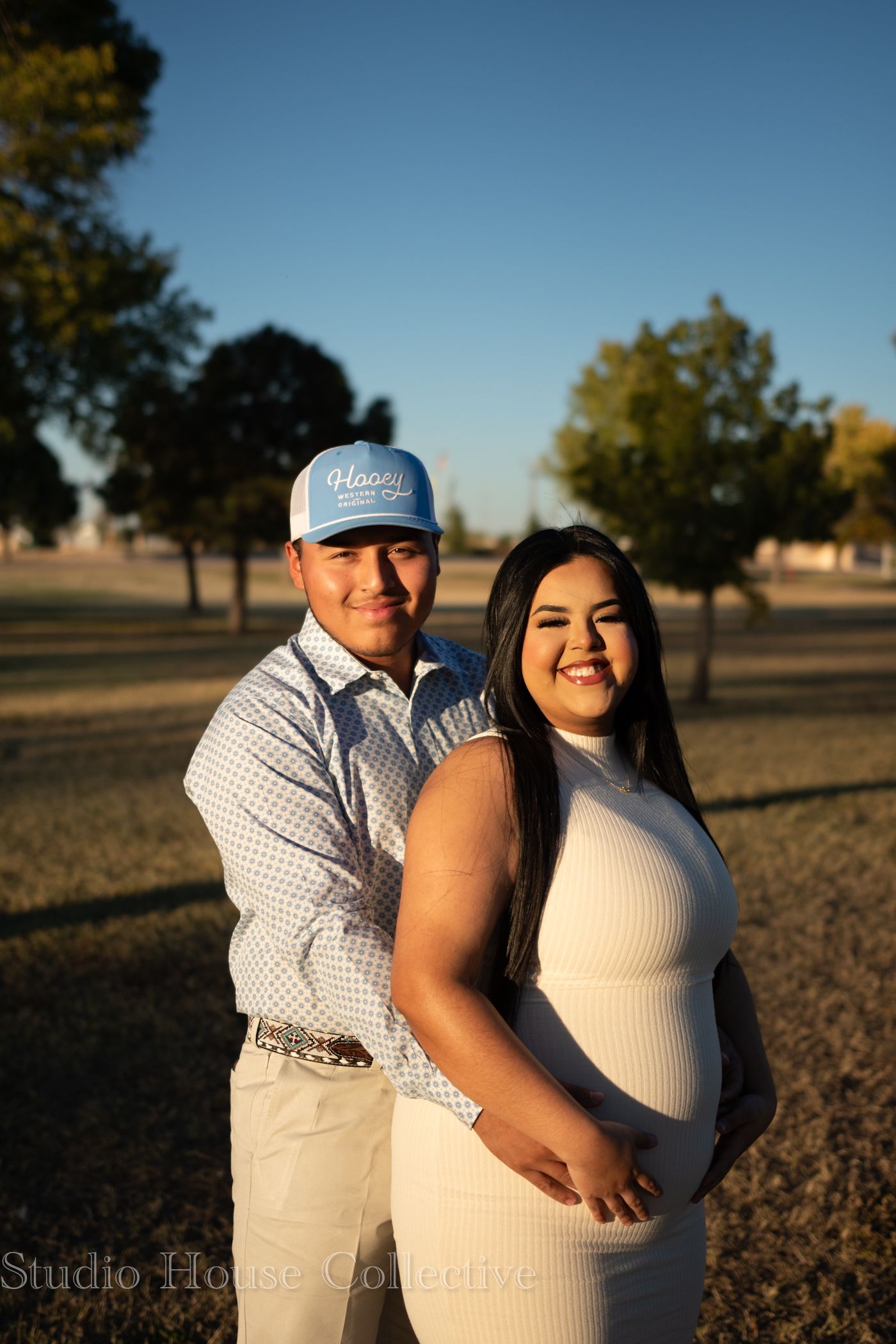 A couple embraces in a golden field during sunset creating a romantic outdoor maternity photoshoot.