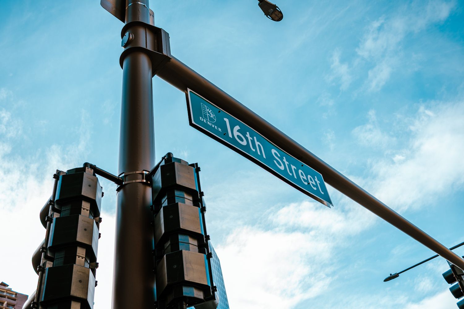 A low angle view of a 16th street sign mounted on a traffic light pole against a bright blue sky.