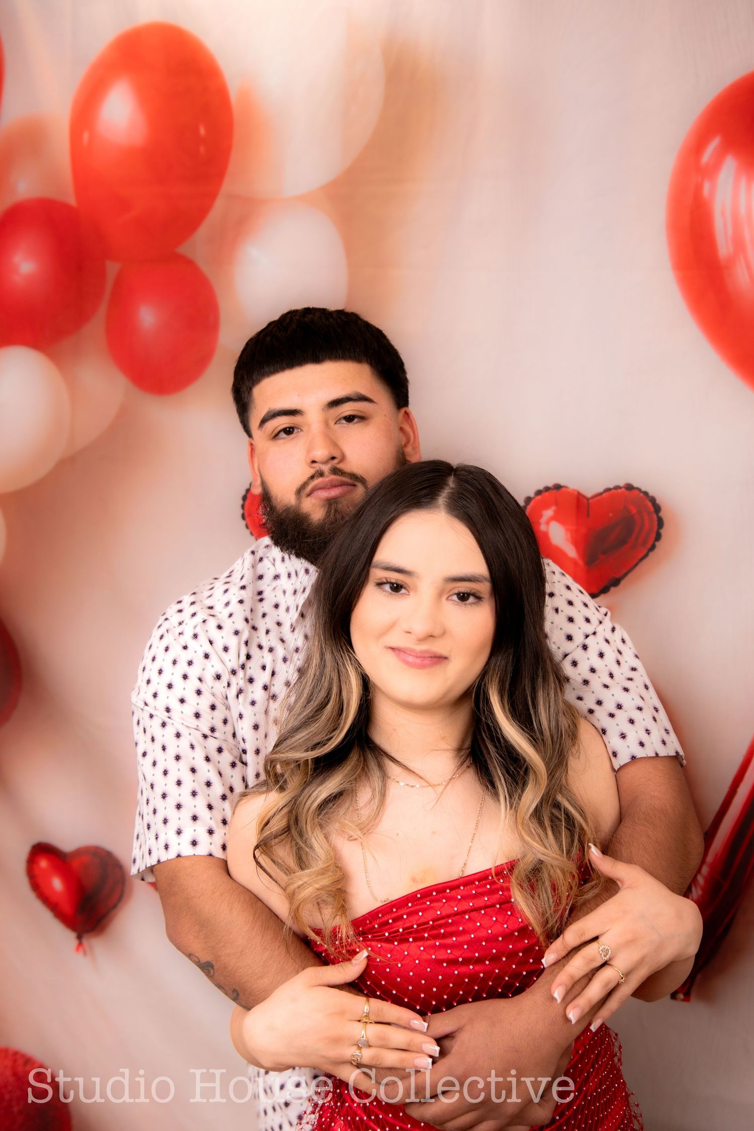 Romantic Valentine's Day photoshoot with red and white balloons and couple in matching outfits against pink backdrop.