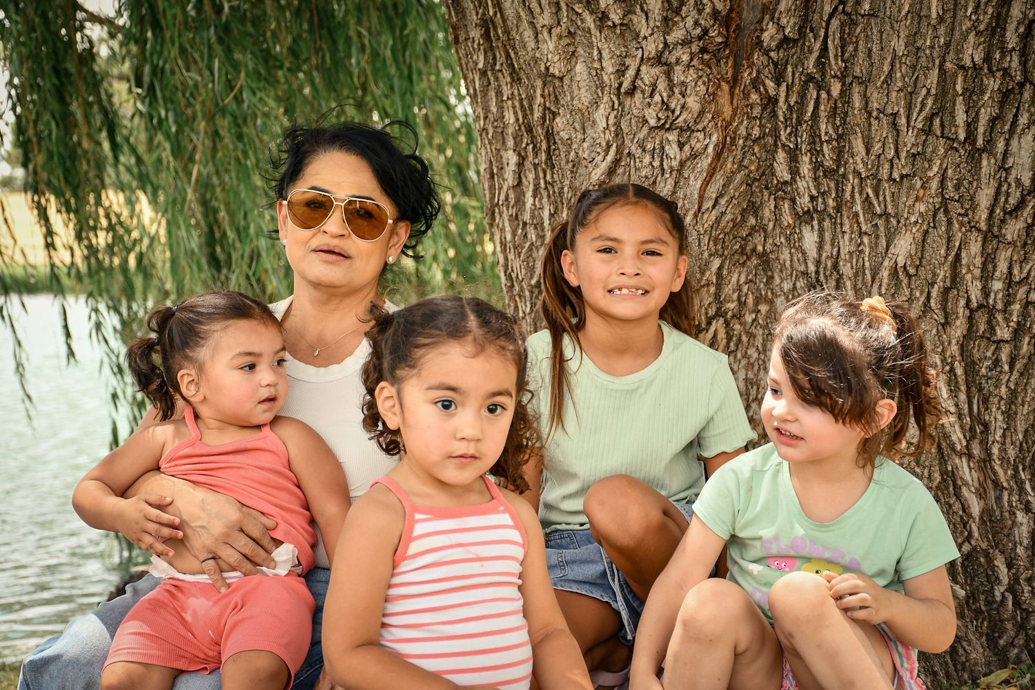 A group poses together under a large willow tree on a bright day.