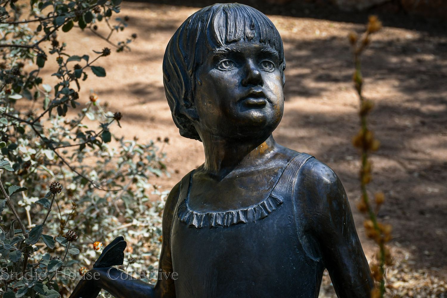 Bronze garden sculpture depicting a child's face with a thoughtful expression in dappled sunlight.