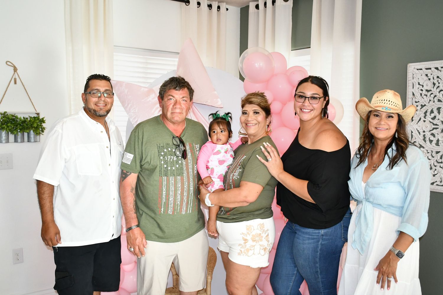 A group gathers at a pink-themed indoor celebration with balloons.