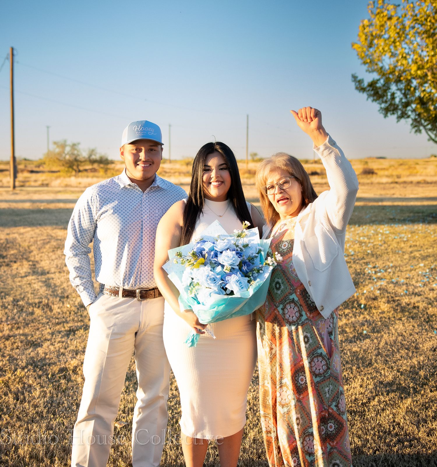 A group stands together in a golden field at sunset wearing coordinated white and blue outfits.