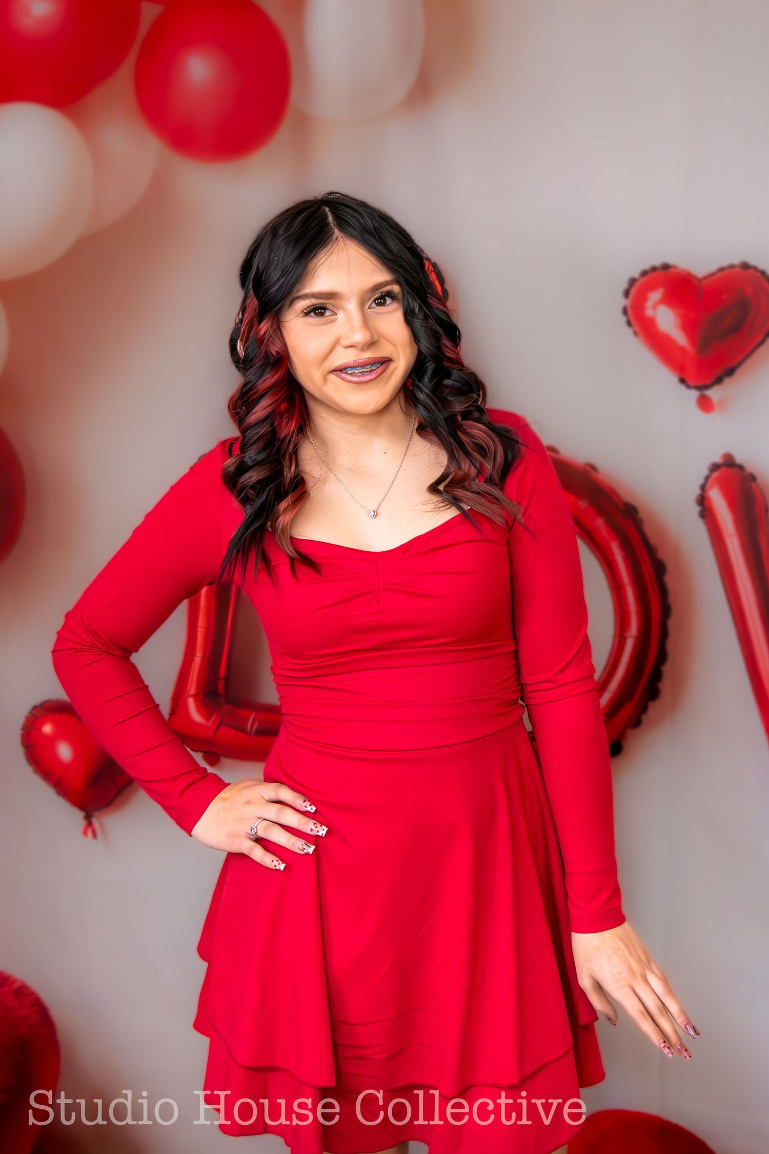 Woman in red dress poses against grey wall with red and white balloon decorations for a studio photoshoot.