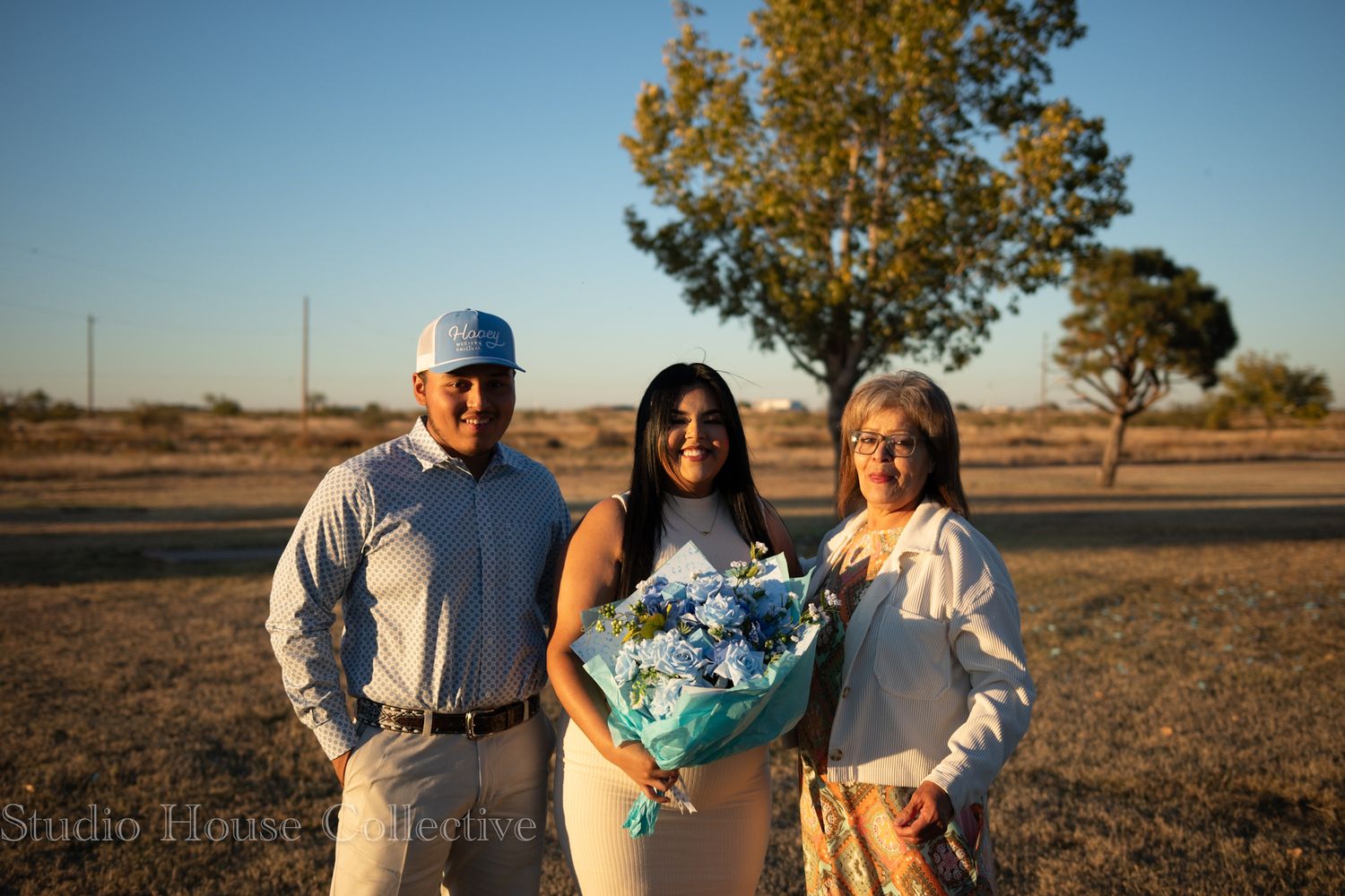 People standing in an open field holding decorative floral bouquets at sunset.