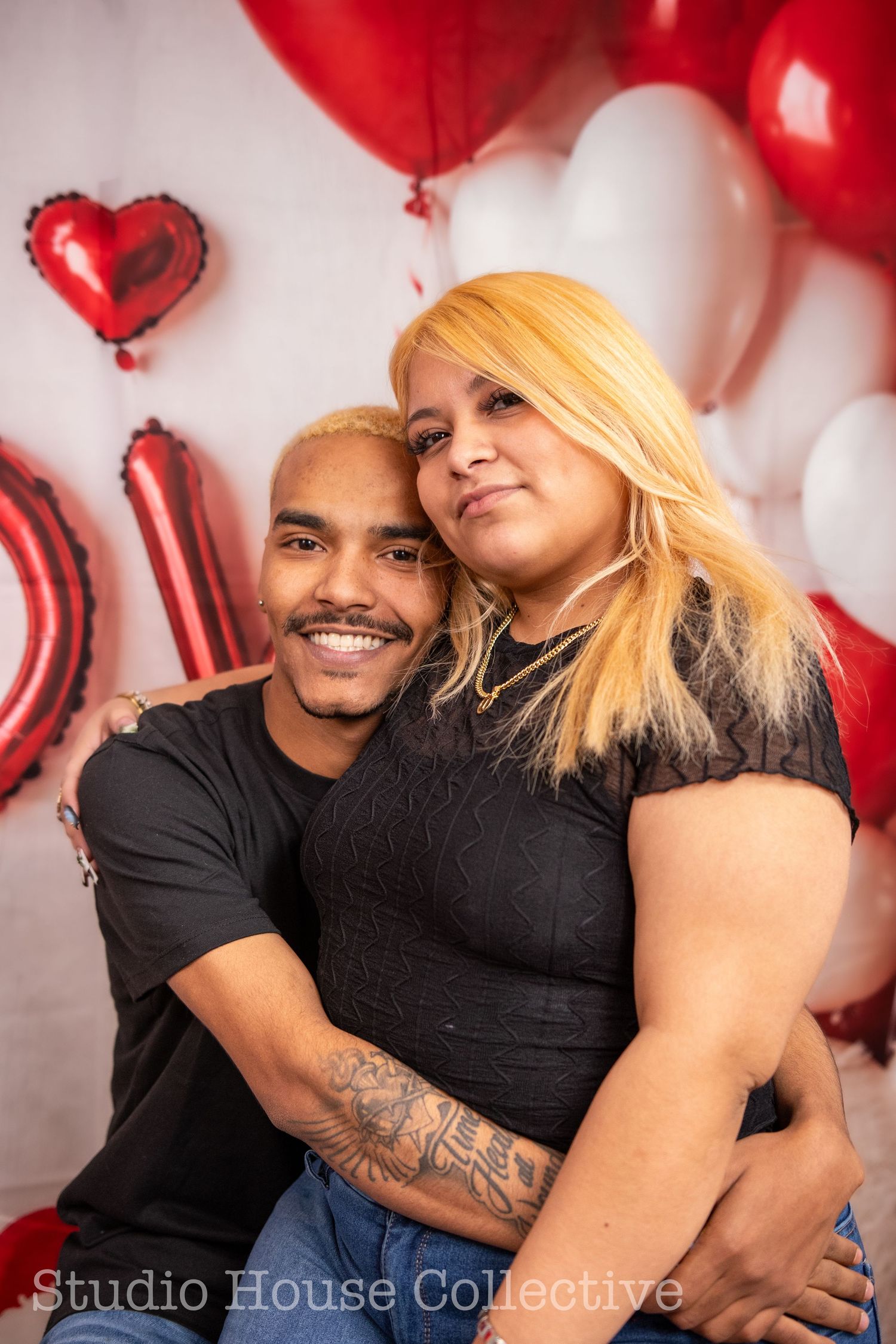 A couple embraces against a backdrop of red and white balloons in a romantic Valentine's Day photoshoot.