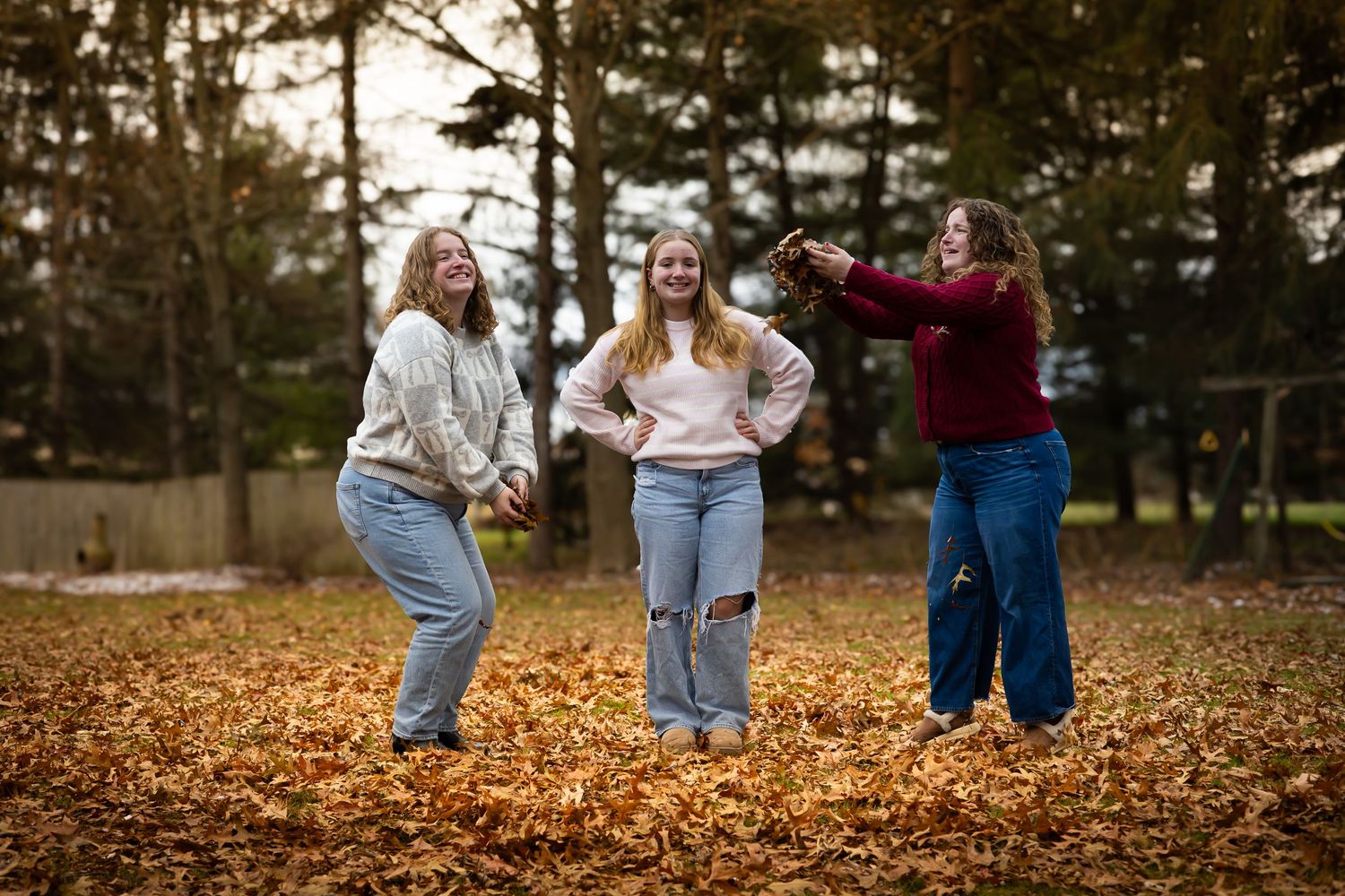 Three young ladies playing with fallen leaves in their backyard.