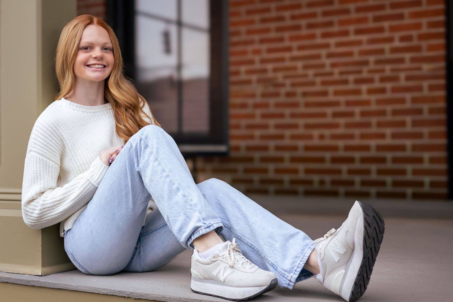 A portrait of a young lady leaning on a beam with a brick background.