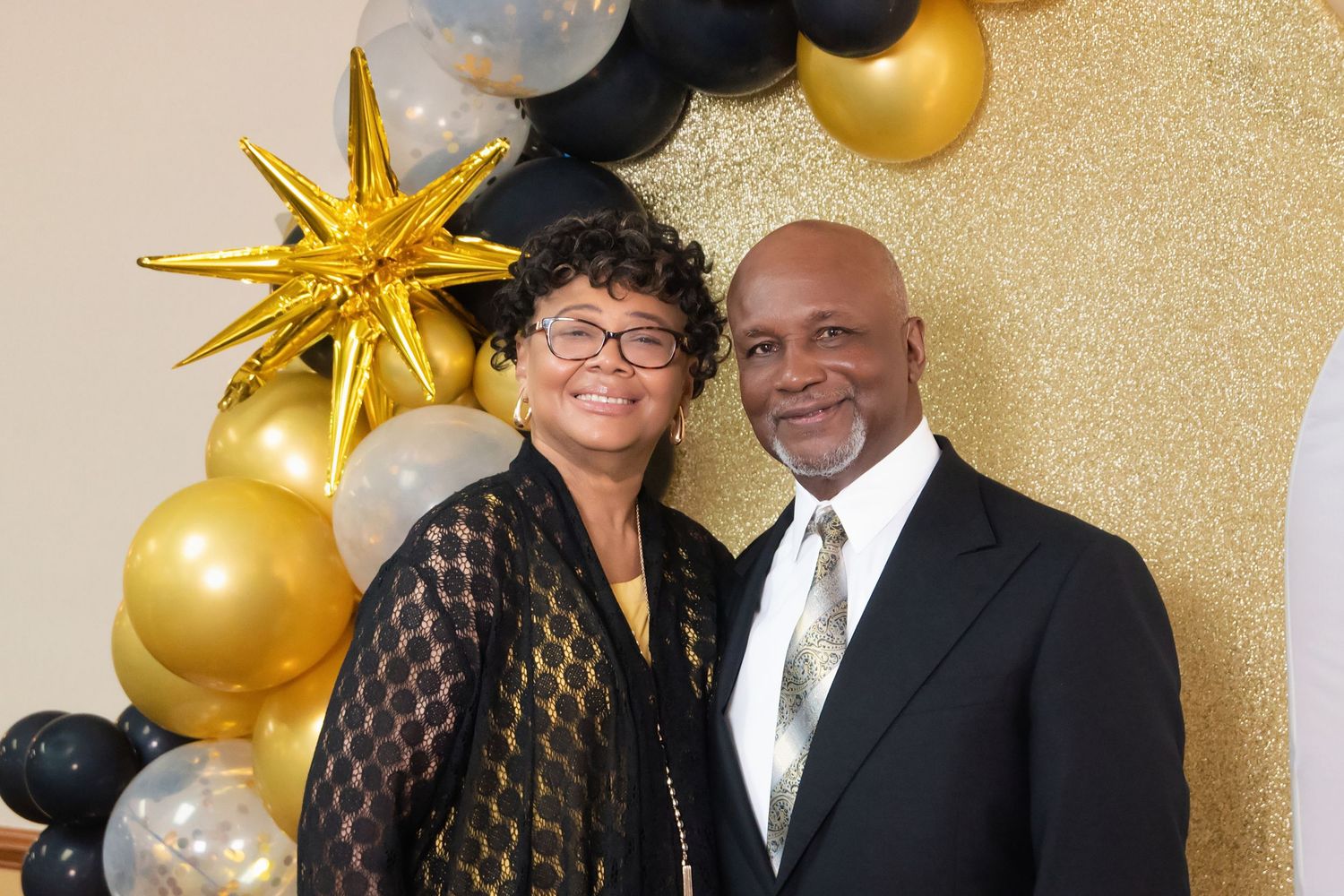 Couple smiling in front of gold, black, and silver balloon arch with star decoration at formal event.