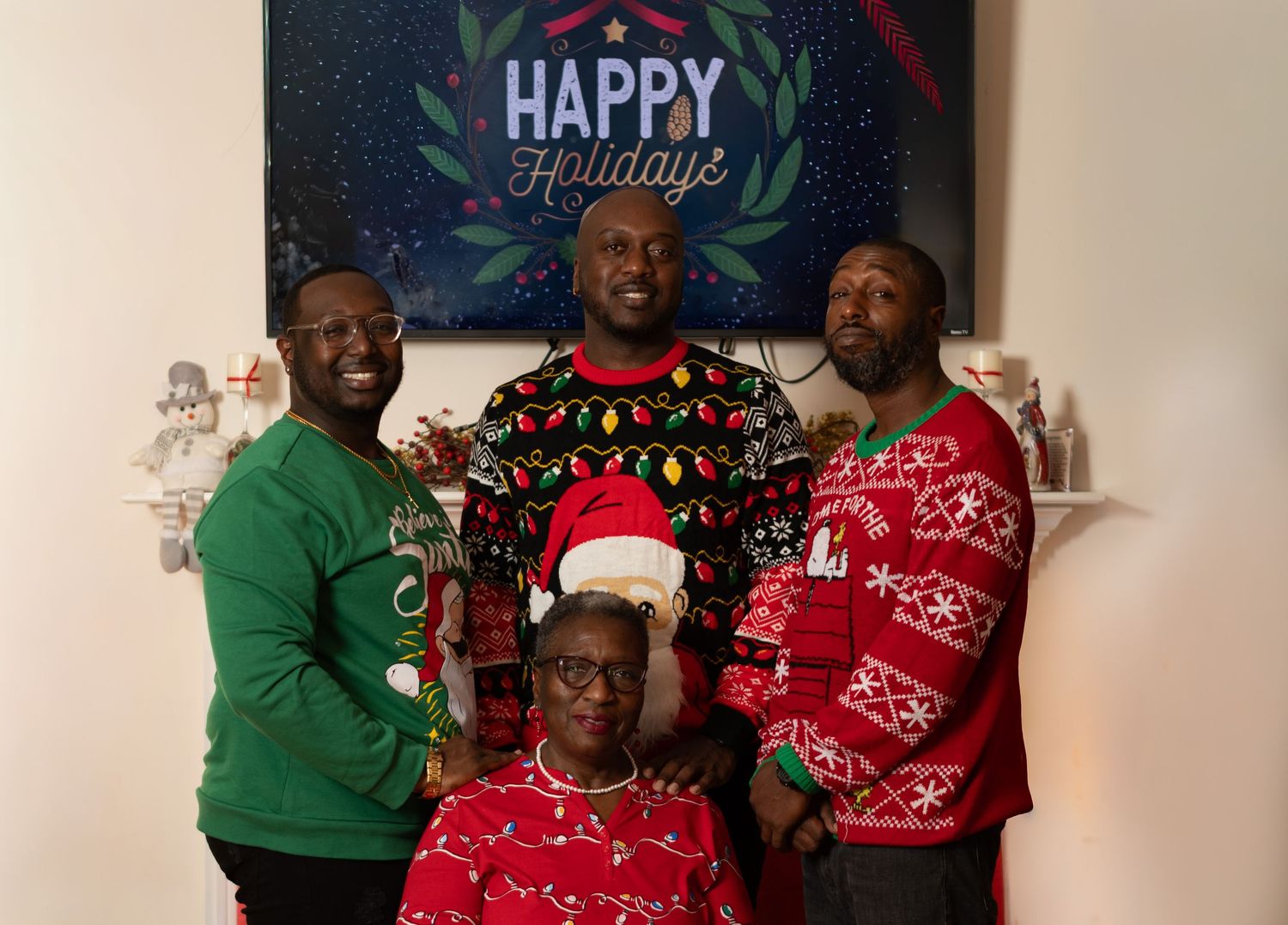 Holiday gathering with people wearing festive Christmas sweaters against Happy Holidays backdrop.