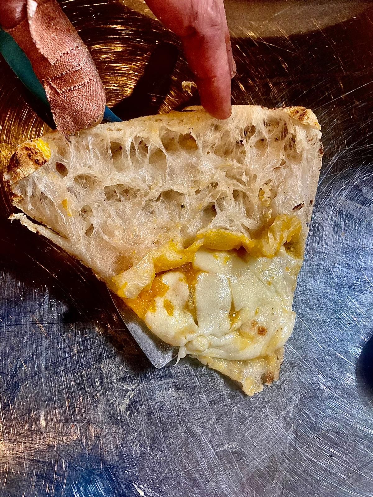 Cross-section of Neapolitan pizza slice revealing honeycomb interior dough texture.