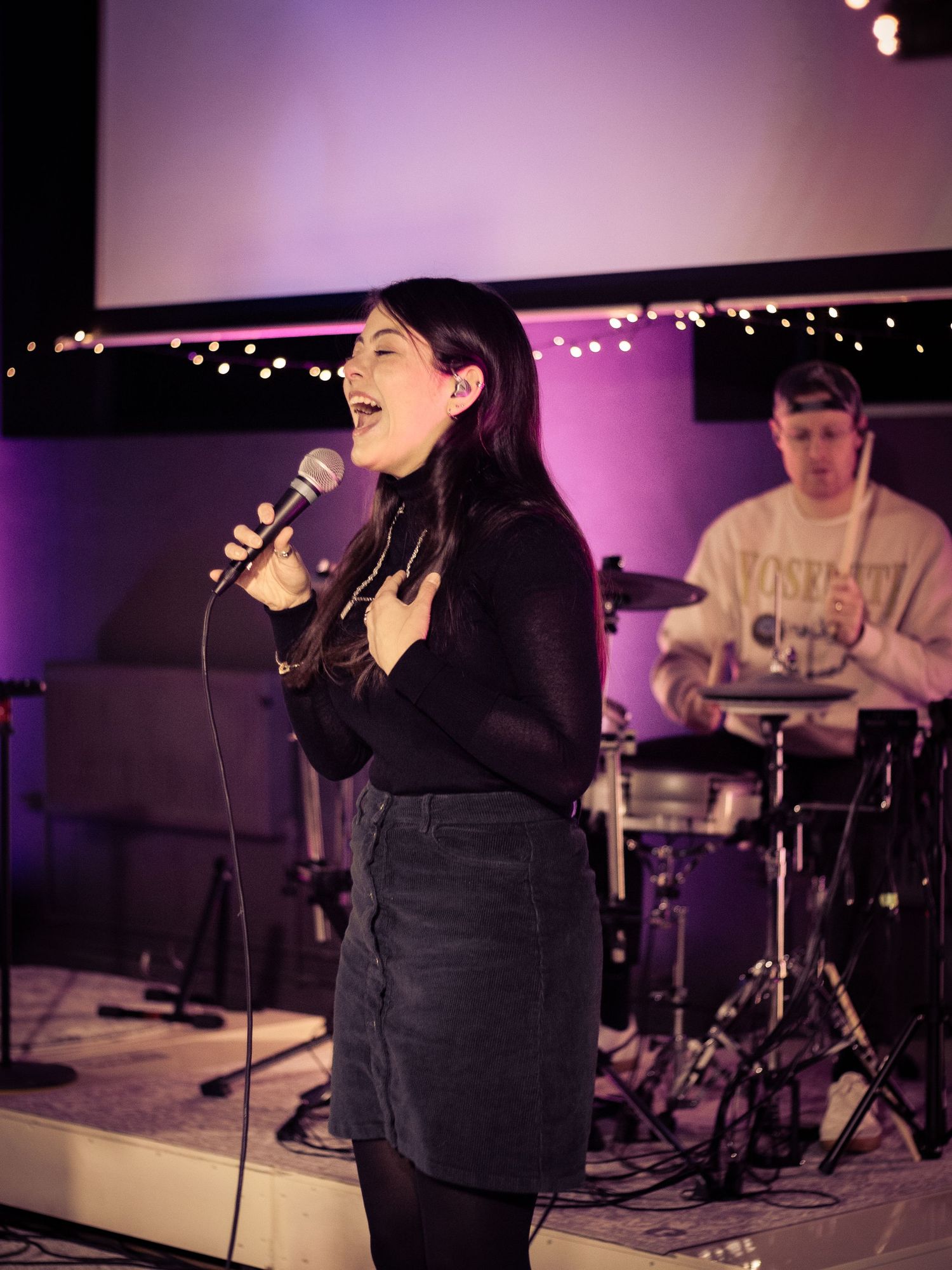 Woman singing on stage and drummer behind her.