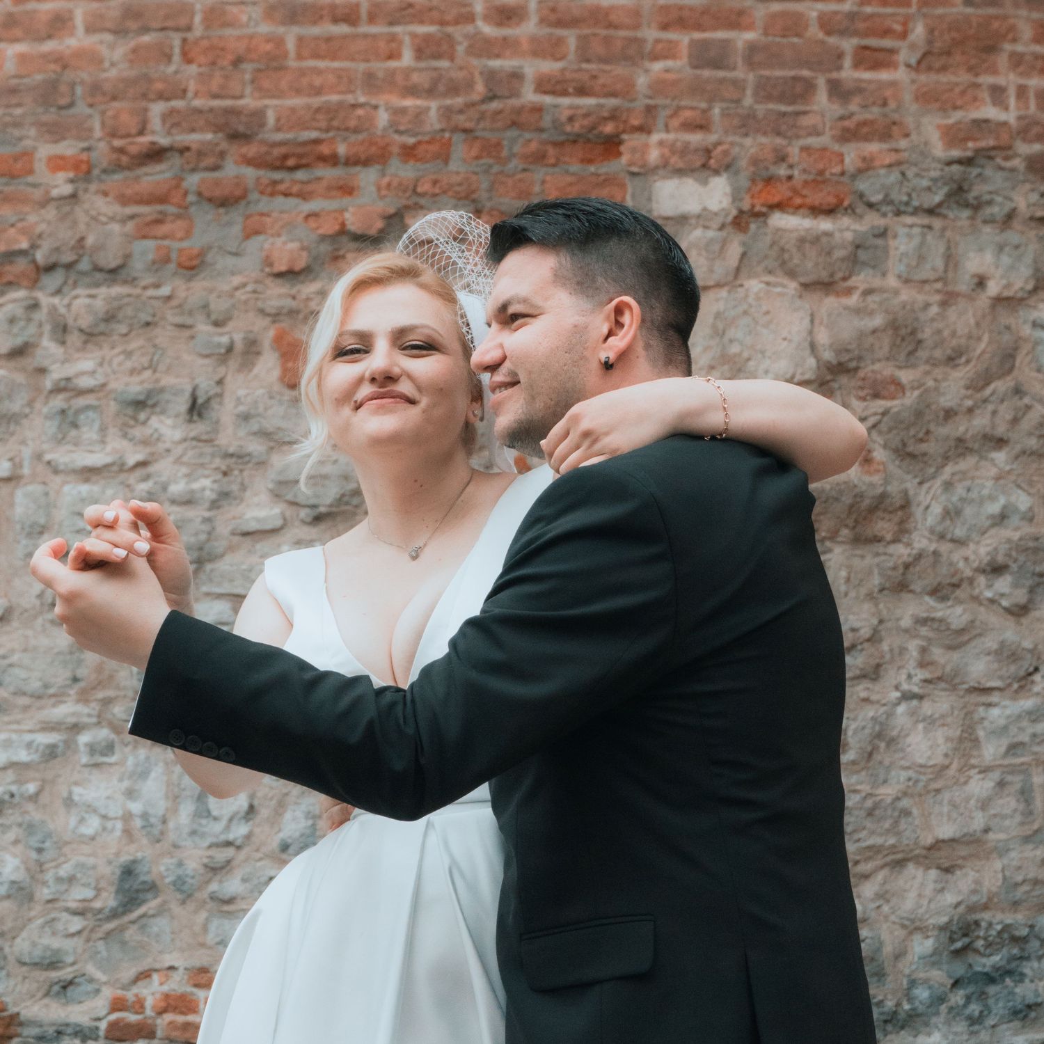 Bride and groom dancing together in front of a rustic brick wall during their wedding celebration.