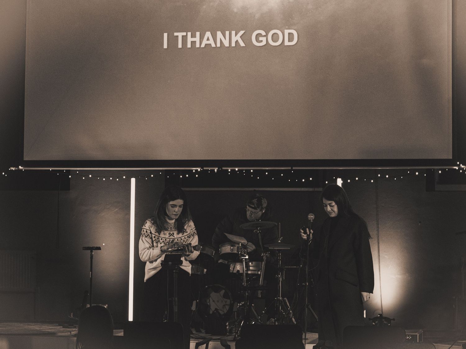 Black and White image of 2 women and a drummer leading Sunday Service, with the words 