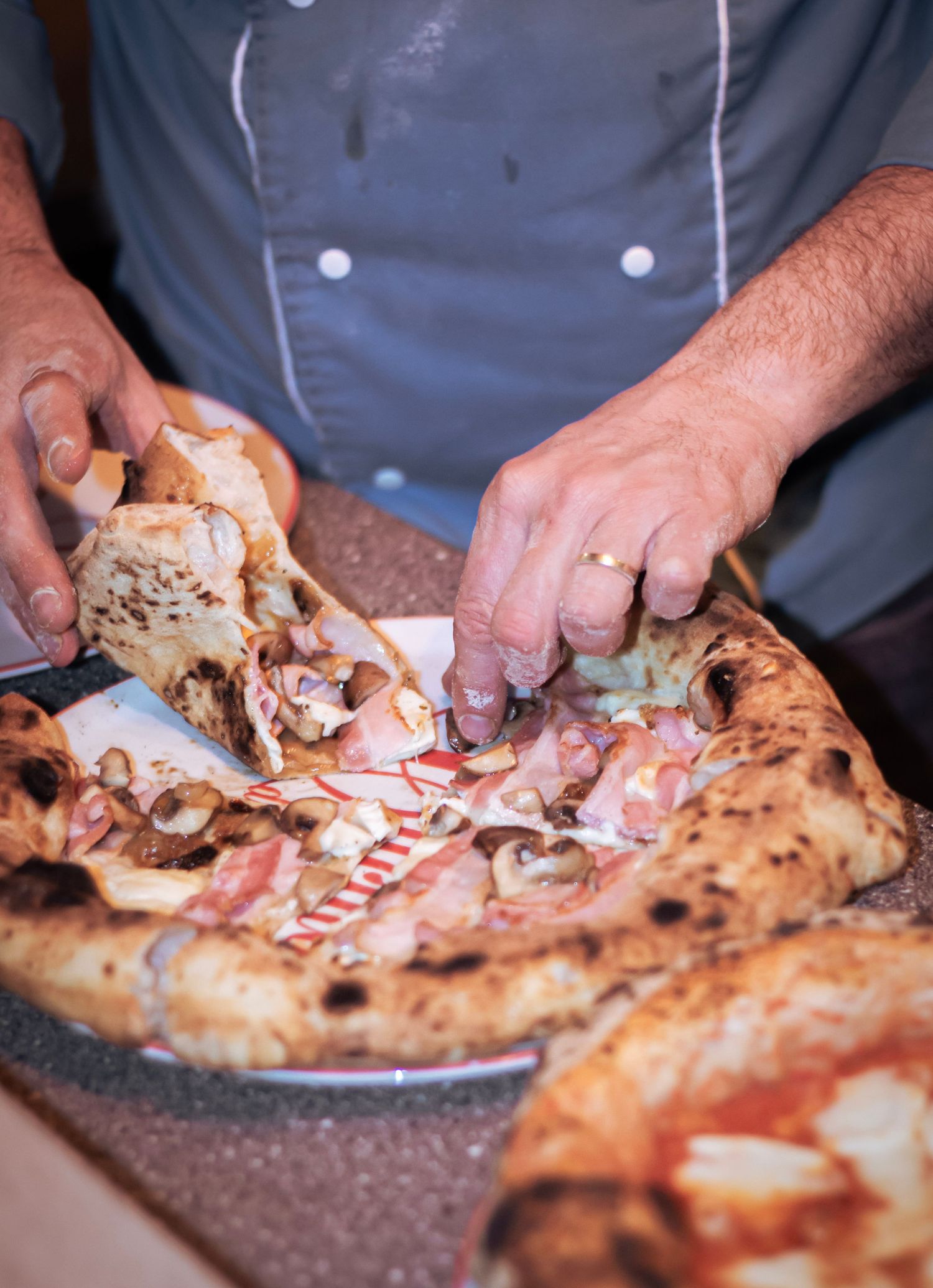 Chef hands pulling apart a freshly baked Neapolitan pizza with prosciutto and mushrooms.