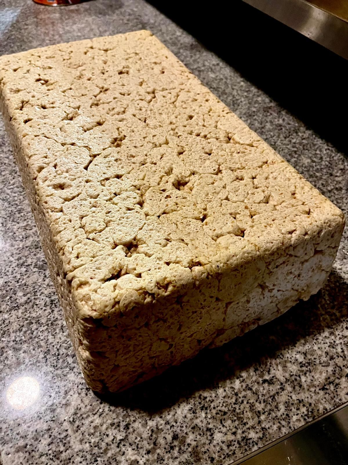 A rectangular block of firm tofu with a rough, porous surface resting on a dark granite countertop.