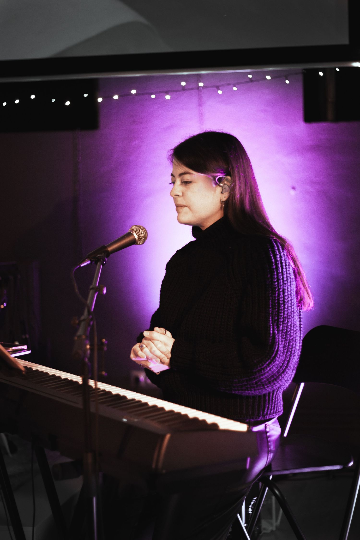Woman sitting at a keyboard with purple spotlight behind her.