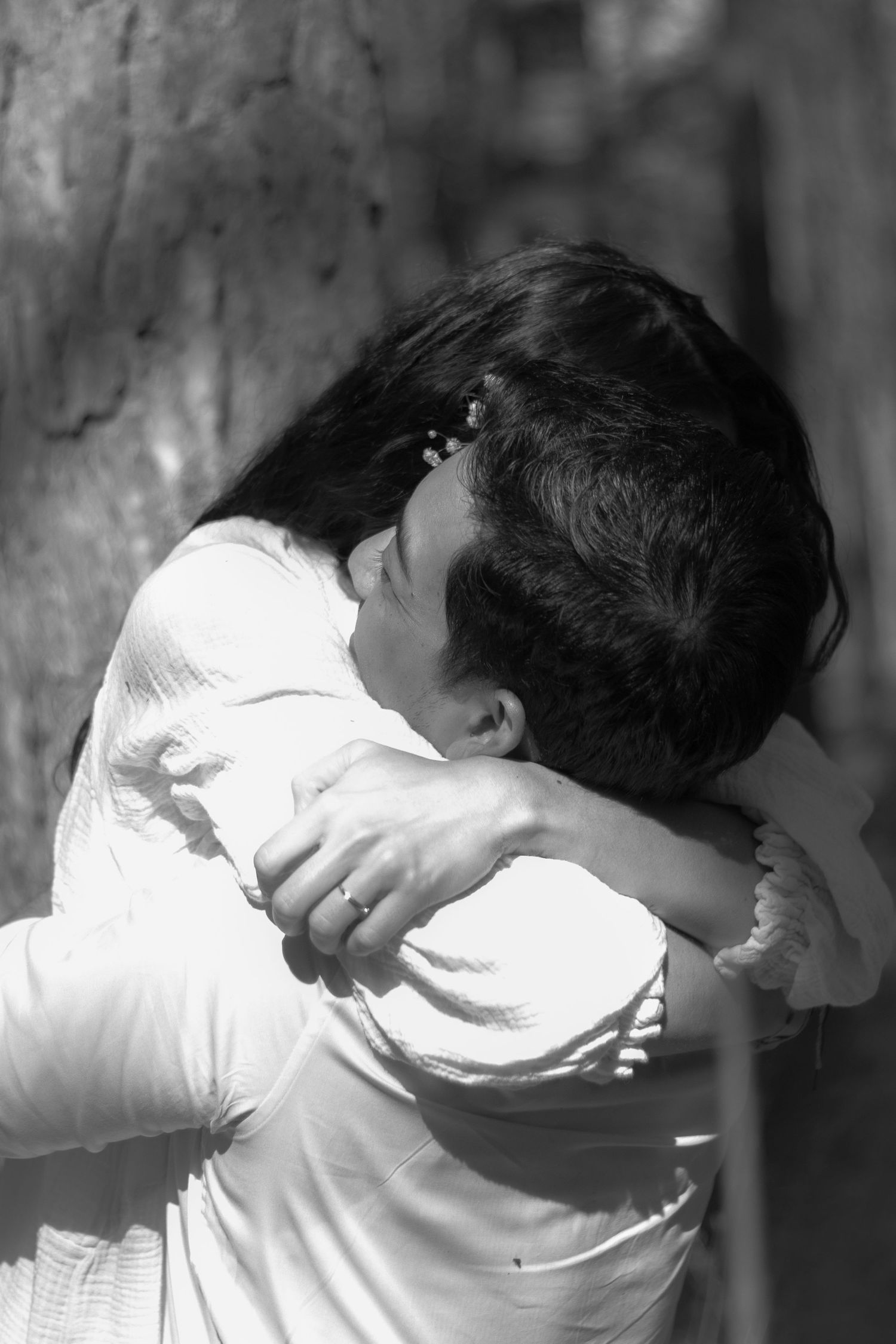 Couple embracing tenderly against tree in black and white romantic outdoor photo.