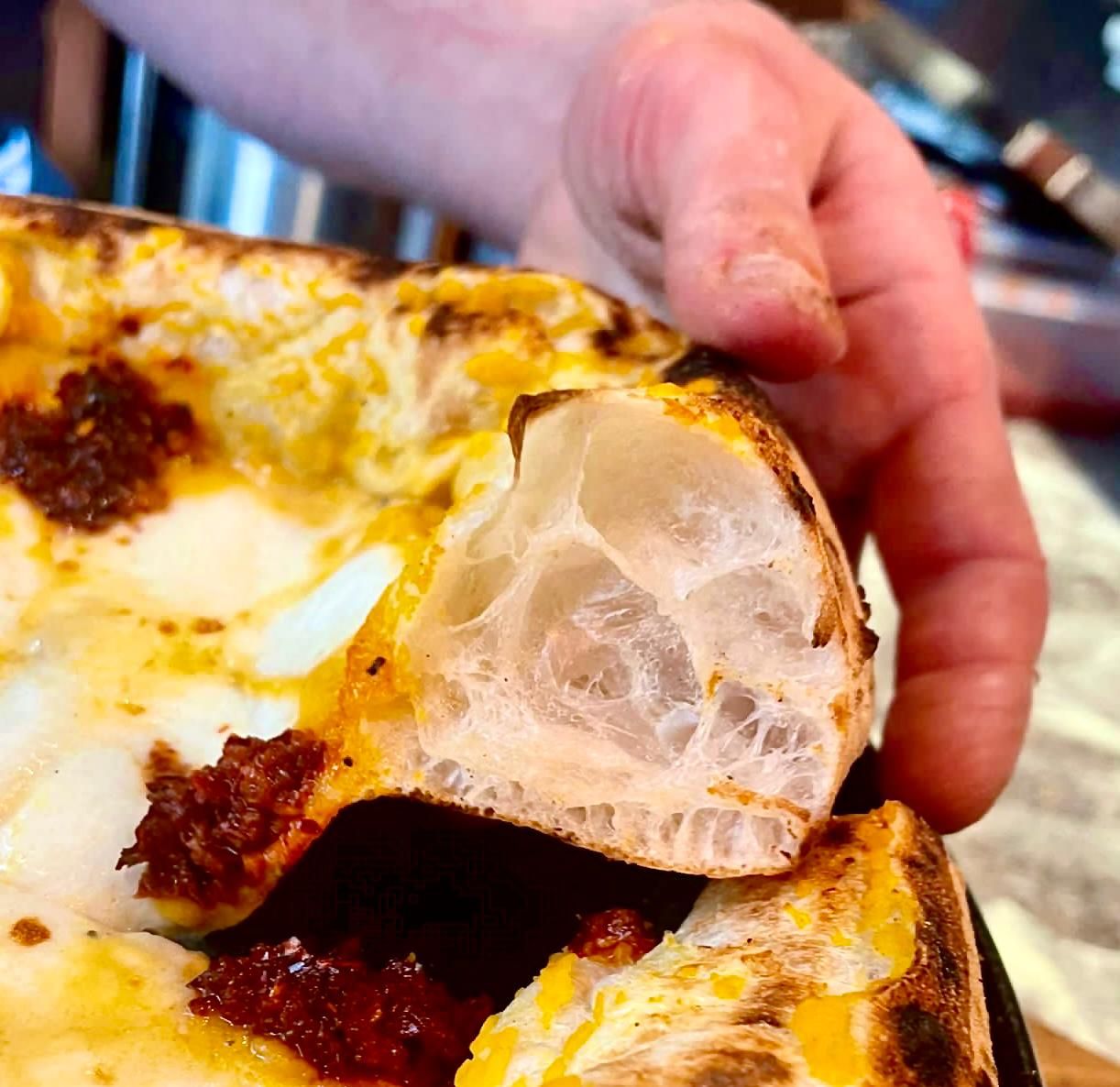 Close-up of pizza crust cross-section showing large air bubbles in baked dough.