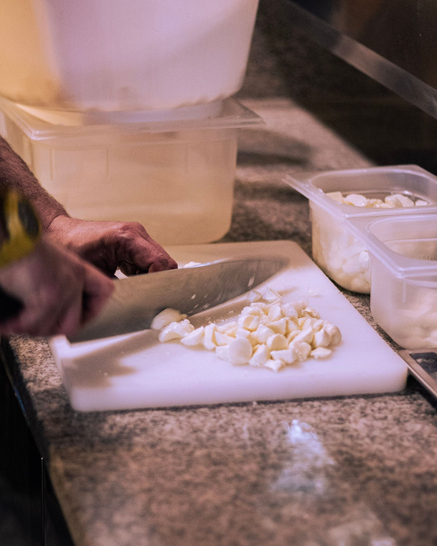 Chef slicing fresh mozzarella on a white cutting board in a professional kitchen.