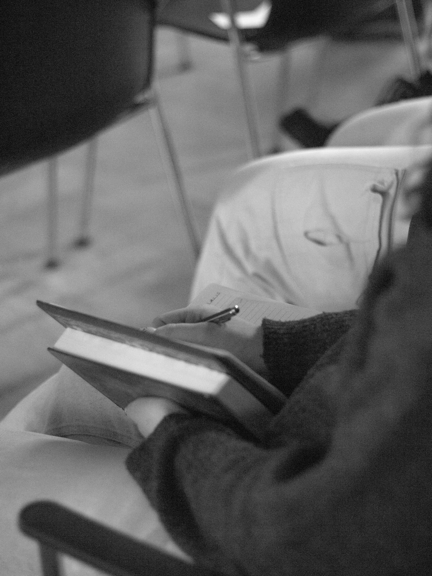 Black and white photo of a young person sitting holding a notebook and pen in hand.