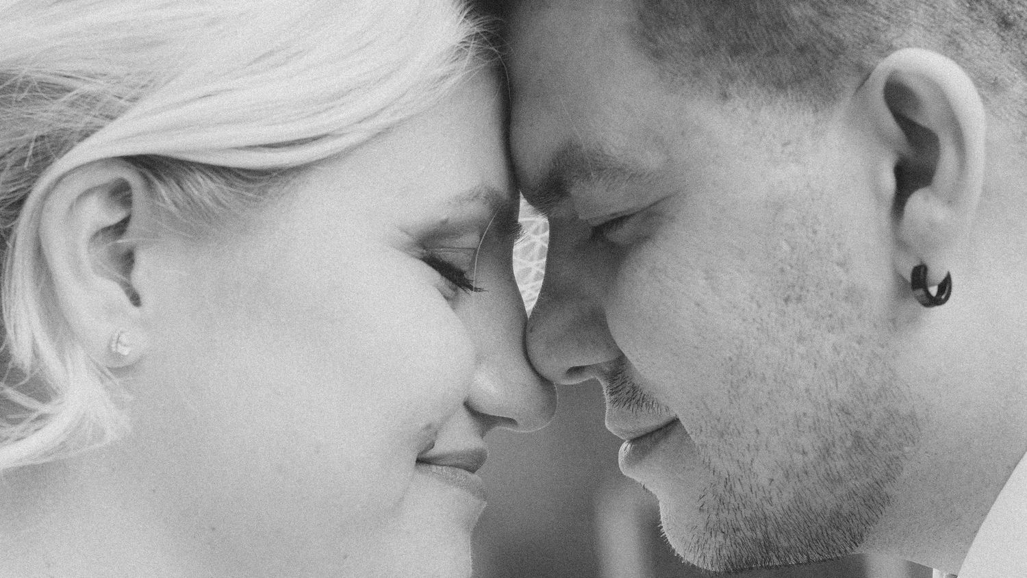 Black and white close-up of a romantic couple touching foreheads, smiling tenderly in an intimate portrait.