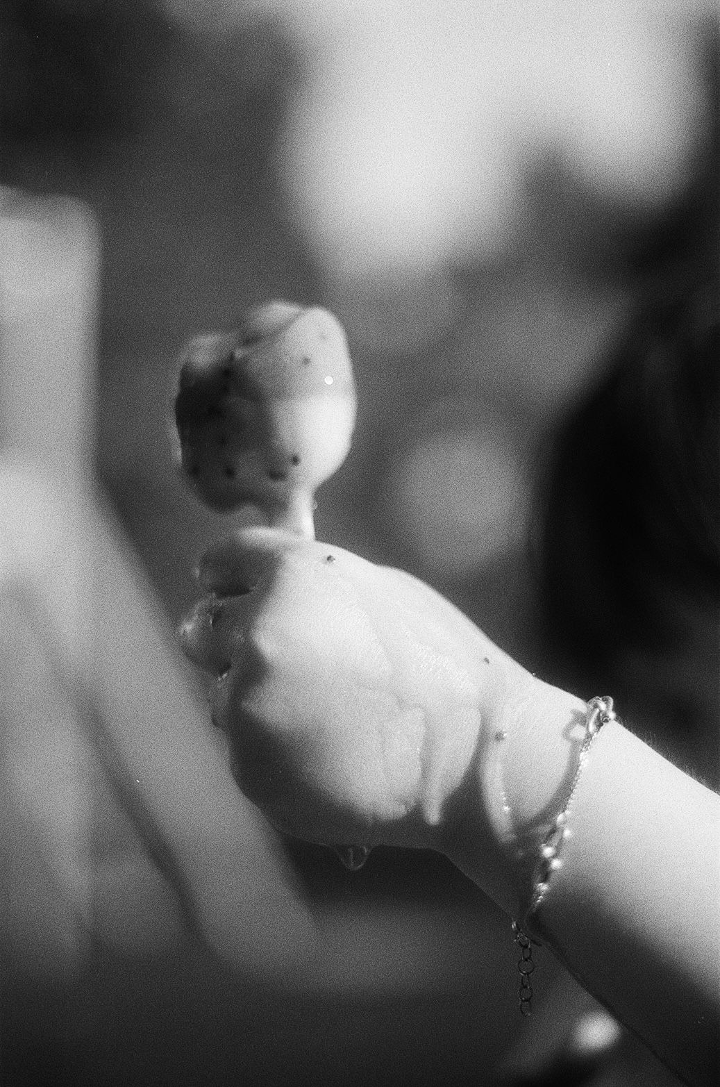 Black and white photo of a hand wearing a delicate chain bracelet holding a melting popsicle.