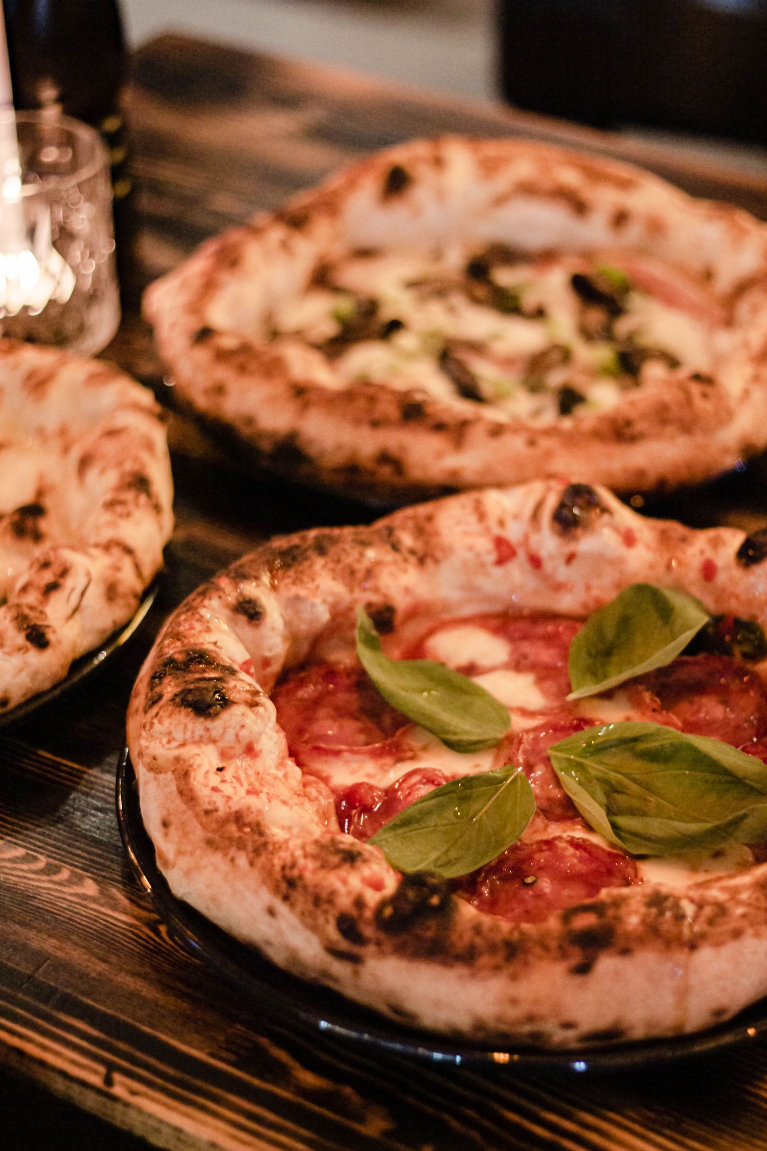 Two Neapolitan pizzas topped with fresh basil and tomato sauce on a wooden table.