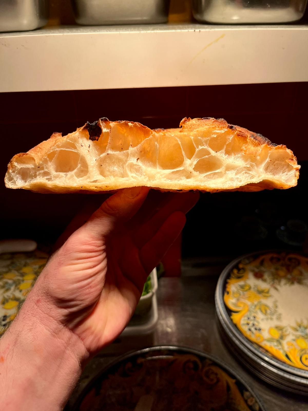 Hand holding pizza crust cross-section revealing golden honeycomb air pocket texture.