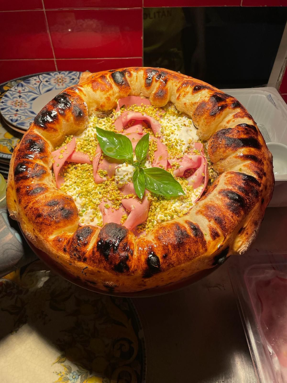 Artisan ring-shaped pizza with ham, fresh basil, and cheese toppings on decorative stand.
