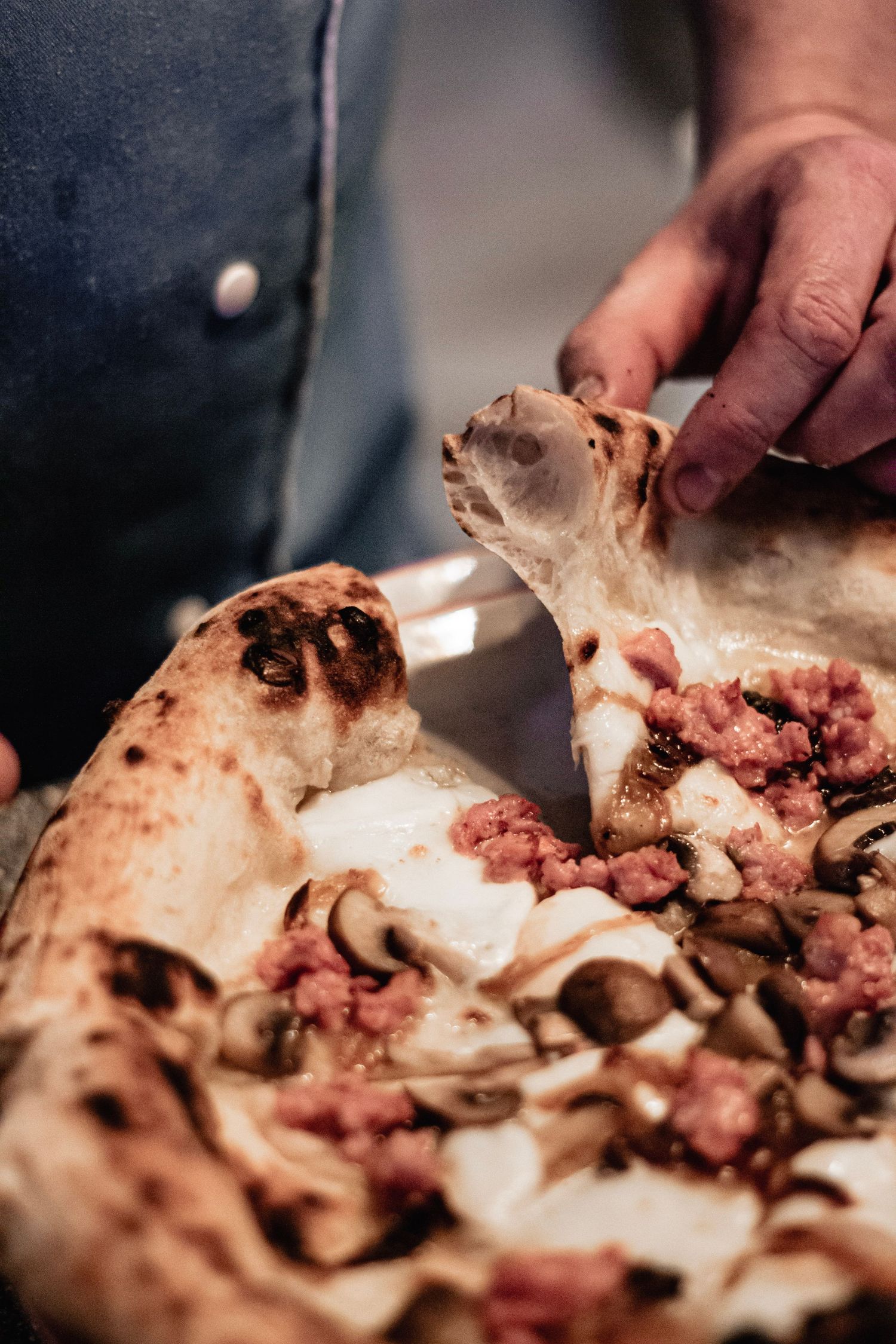 Chef hands cutting a freshly baked Neapolitan pizza topped with sausage and mushrooms.